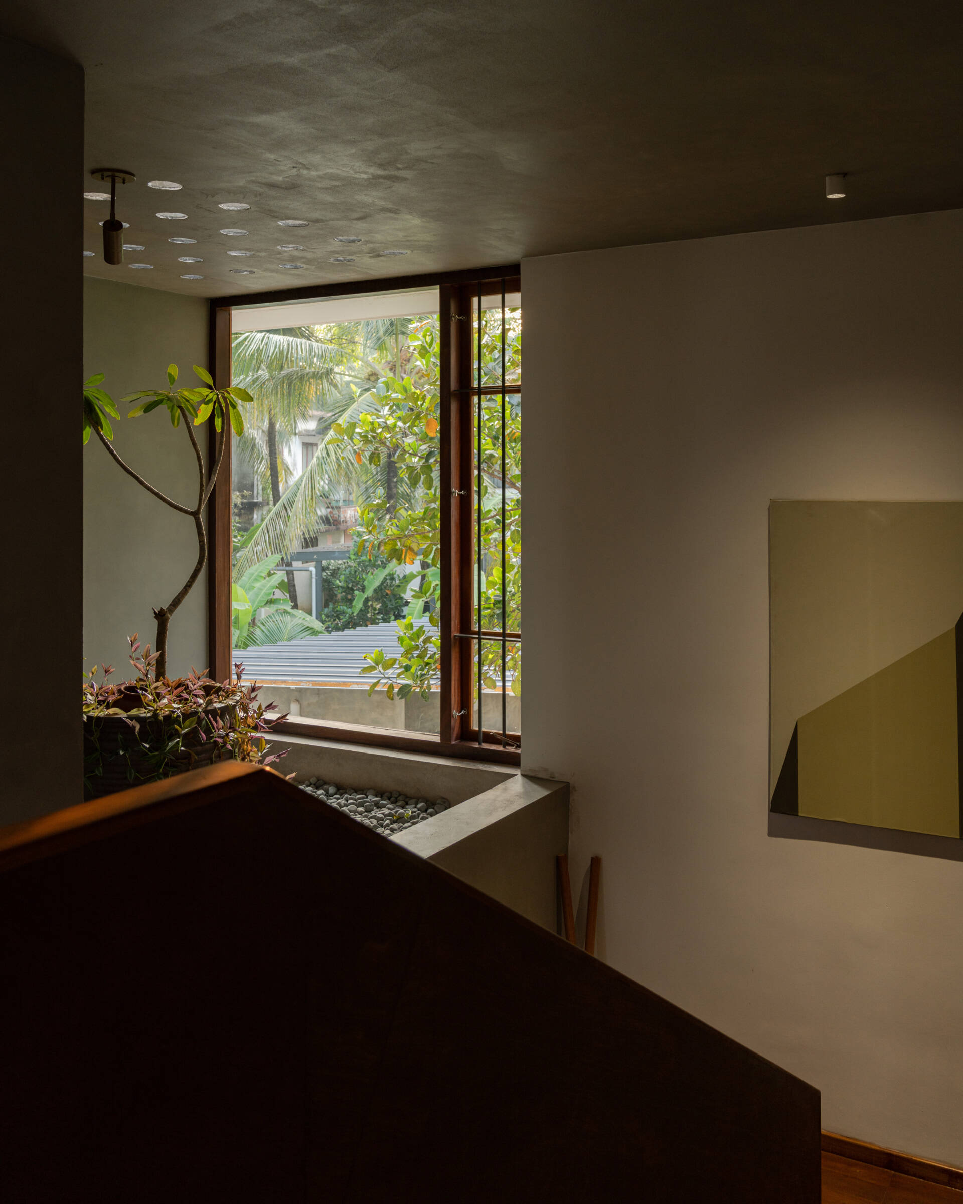 A timber staircase with a solid wooden balustrade and black metal railings links the floors of this contemporary Indian house, overlooking the dining space below.