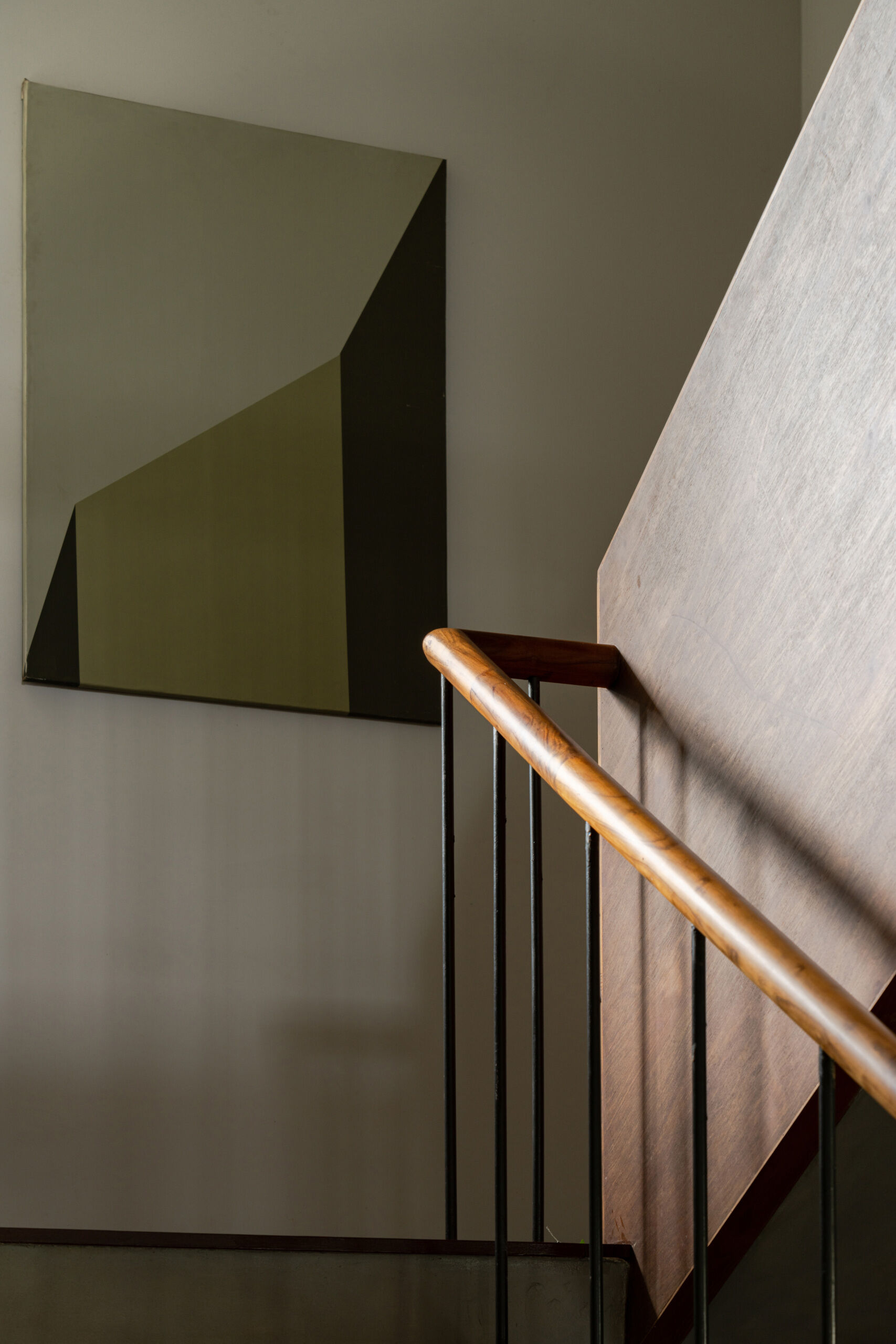 A timber staircase with a solid wooden balustrade and black metal railings links the floors of this contemporary Indian house, overlooking the dining space below.