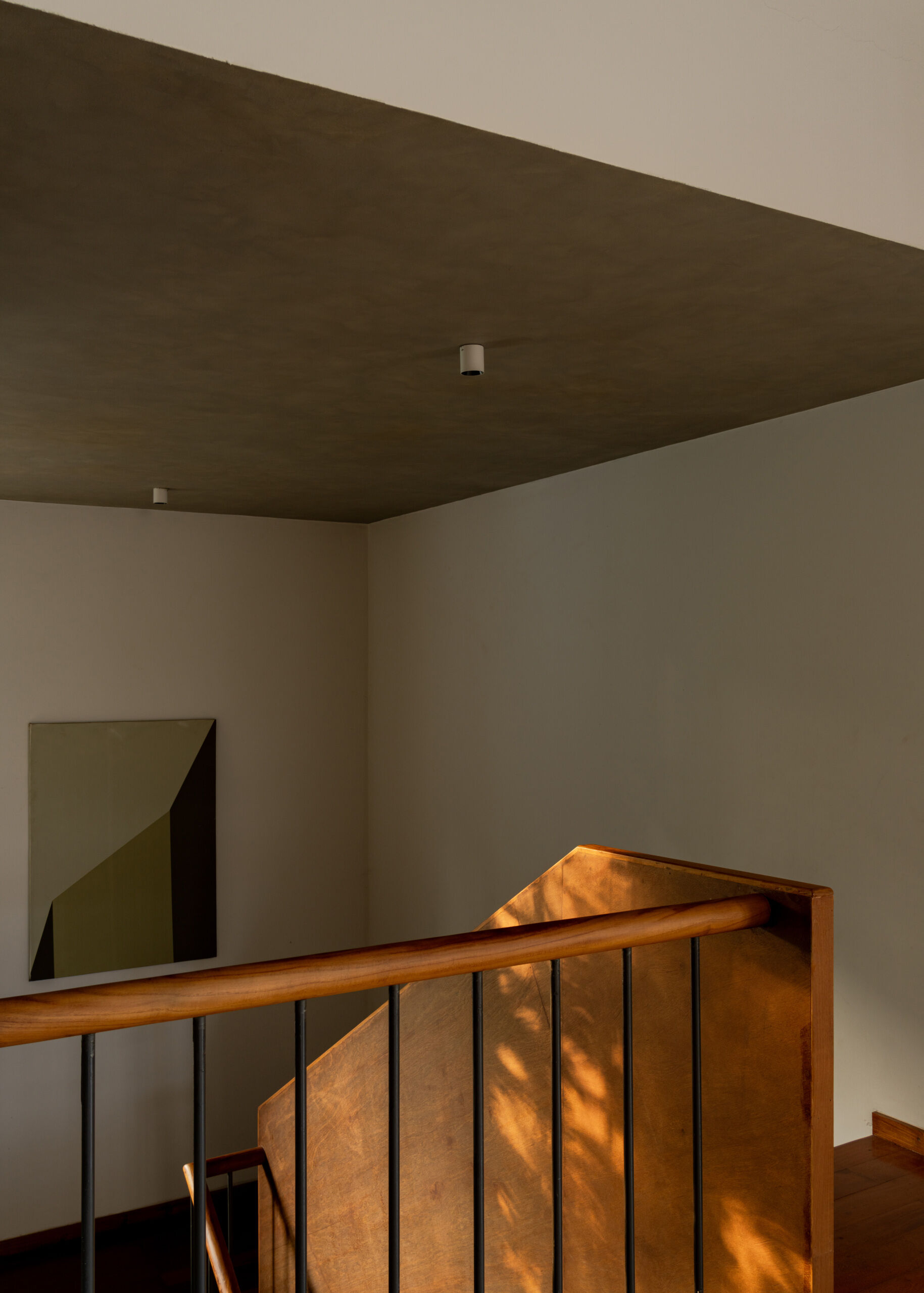 A timber staircase with a solid wooden balustrade and black metal railings links the floors of this contemporary Indian house, overlooking the dining space below.
