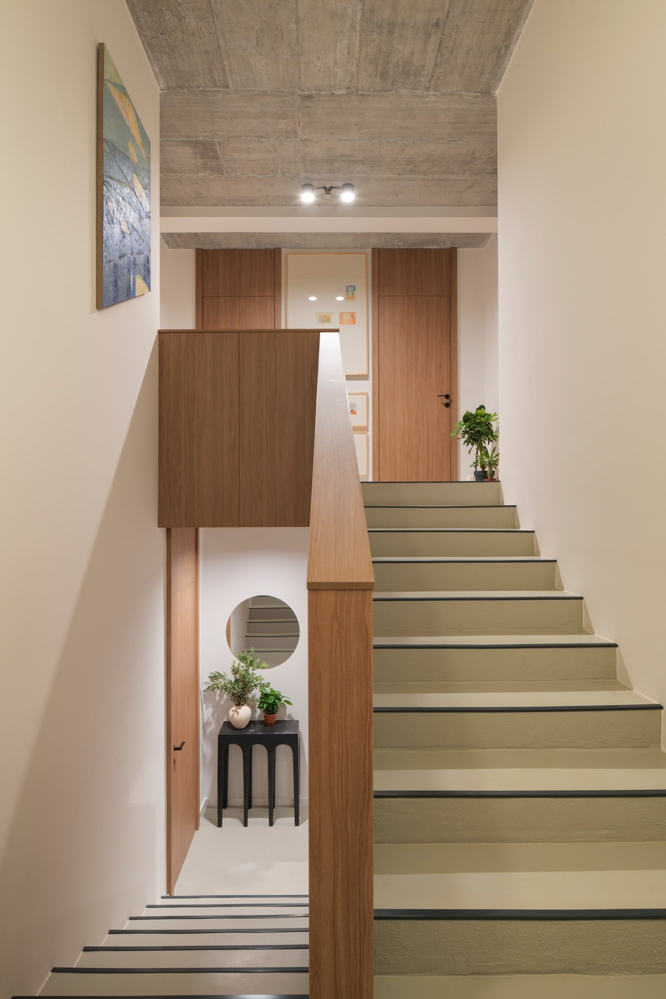 Discover the modern staircase at Arc House, a contemporary Croatian villa, featuring pale green stairs, timber balustrades, exposed concrete ceilings, black architectural lighting and colourful art along the upper landing.