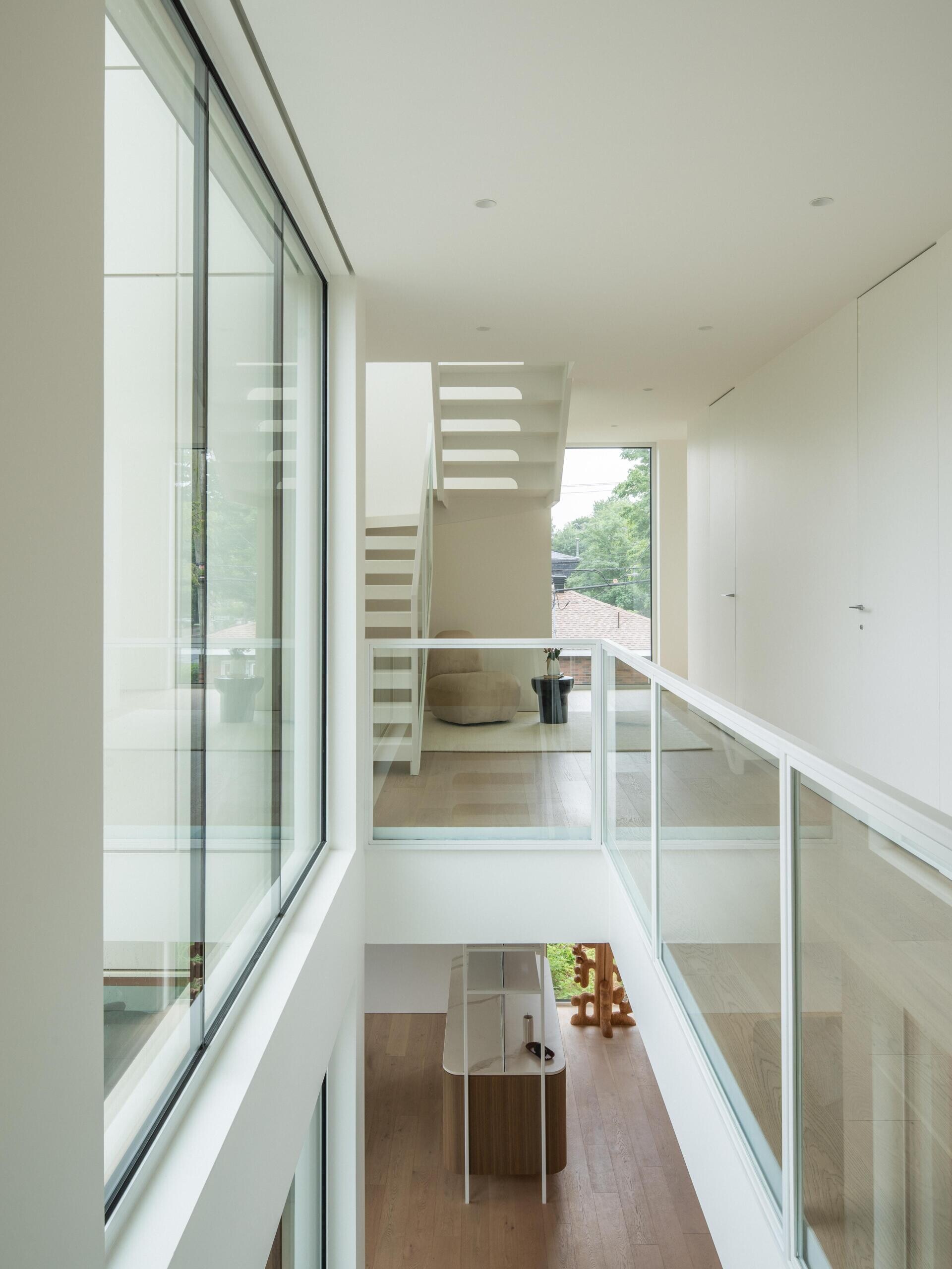 See the floating white steel staircase inside The Lens by MU Architecture in Montreal. Open risers, glass railings, tall windows, and minimalist upper hallways create a bright architectural feature spanning multiple floors.
