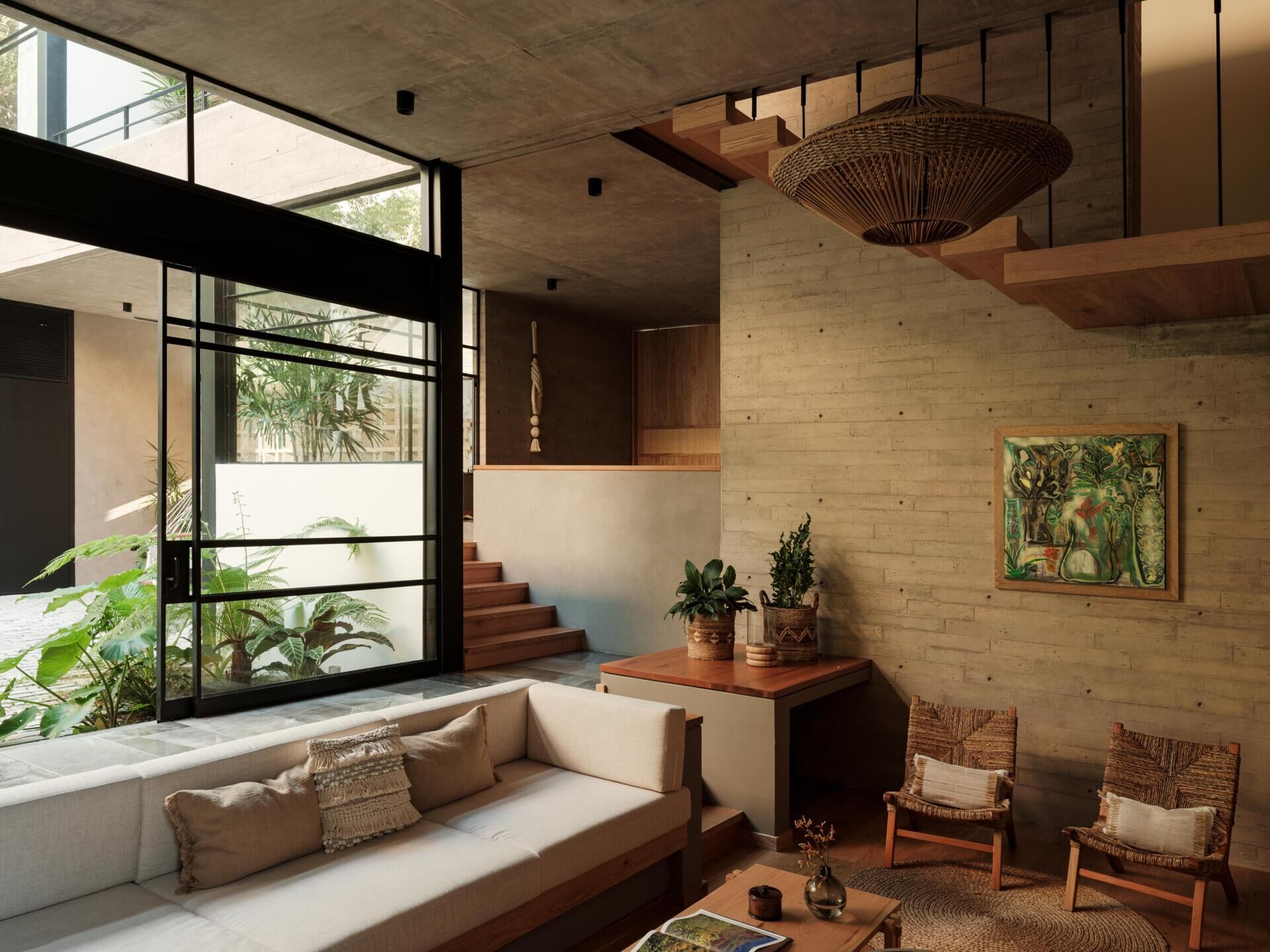 Discover the sunken living room at Casa Akina in Mexico, featuring a built-in L-shaped sofa, custom wood cabinetry, illuminated shelving, woven furniture, and a warm, modern interior design.