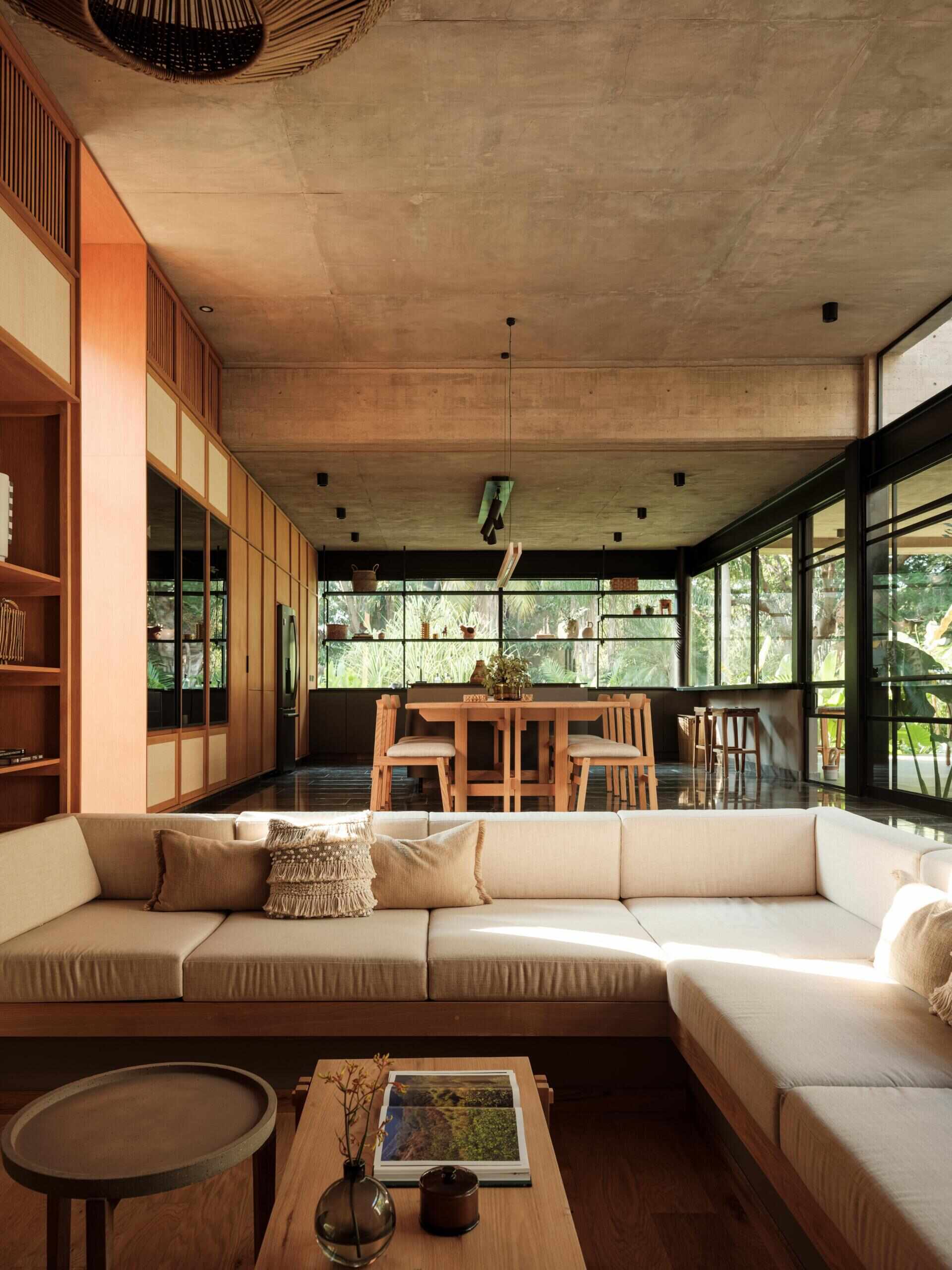 Discover the sunken living room at Casa Akina in Mexico, featuring a built-in L-shaped sofa, custom wood cabinetry, illuminated shelving, woven furniture, and a warm, modern interior design.