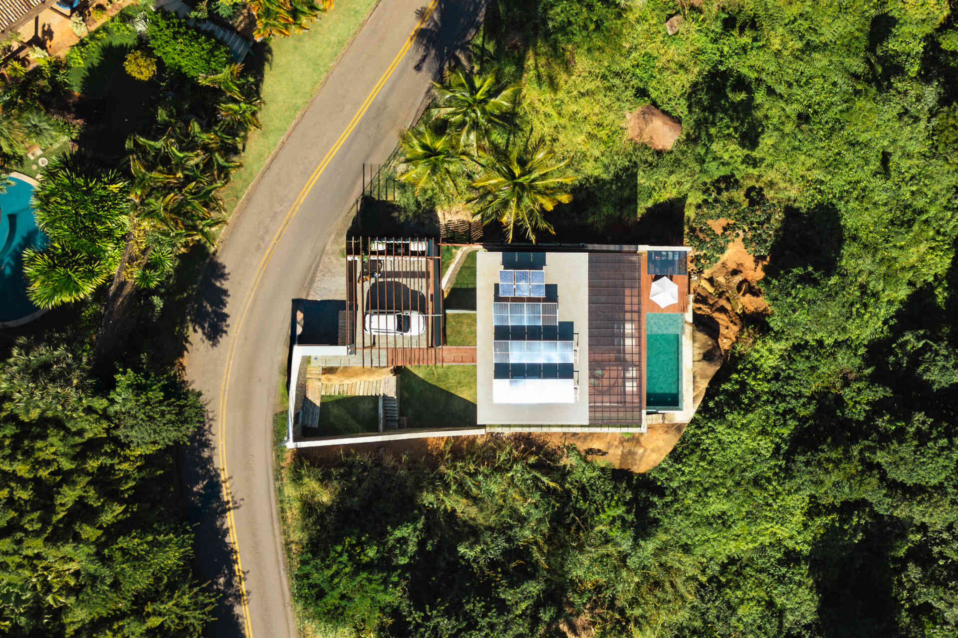 Casa Ponta da Sela in Ilhabela, Brazil, uses prefabricated timber construction, stone retaining walls, glass and timber decks to step down a steep tropical site. Existing rocks, a flat roof with solar systems and an elevated pool become part of the architecture.
