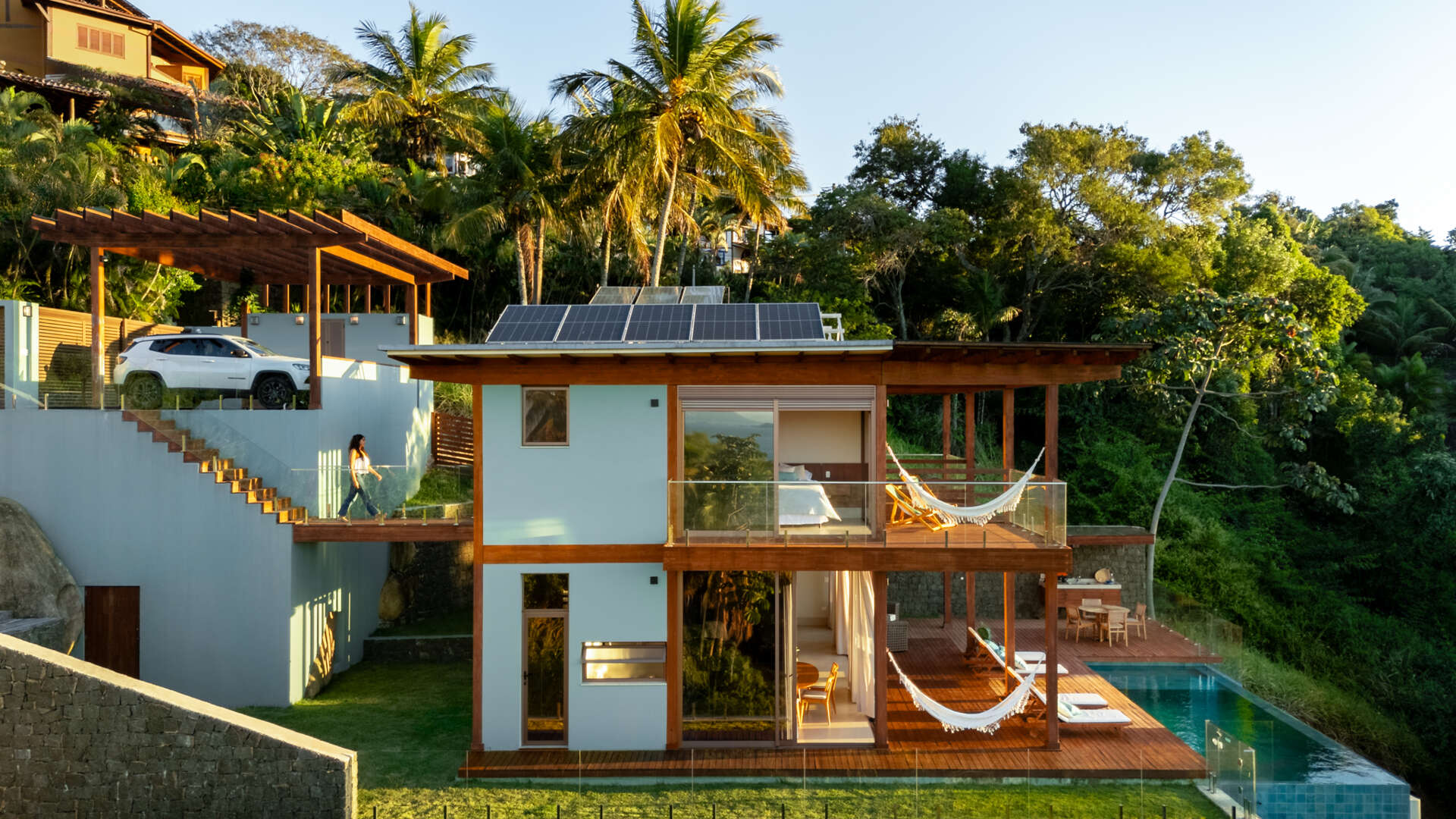 Casa Ponta da Sela in Ilhabela, Brazil, uses prefabricated timber construction, stone retaining walls, glass and timber decks to step down a steep tropical site. Existing rocks, a flat roof with solar systems and an elevated pool become part of the architecture.