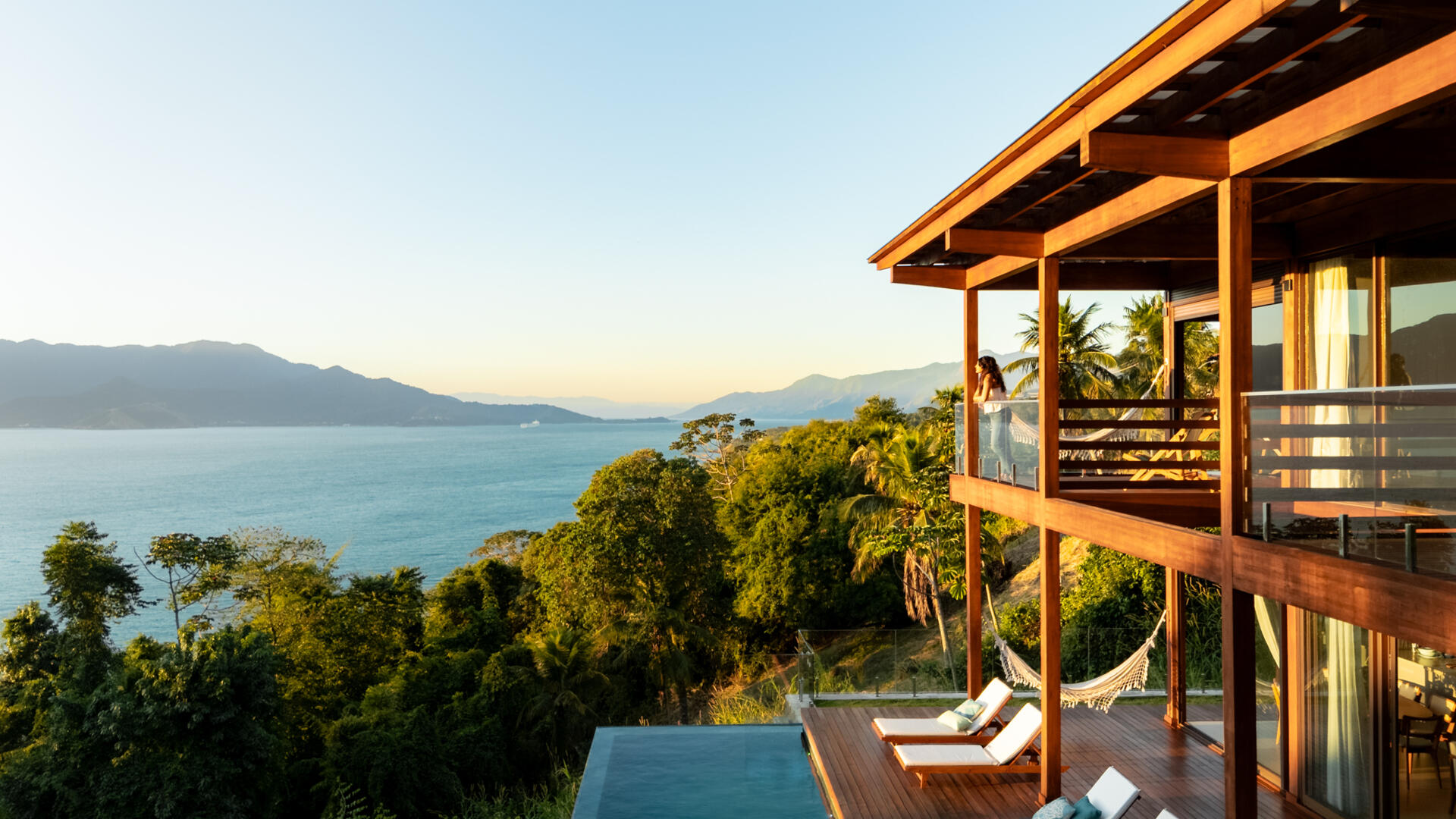 Casa Ponta da Sela in Ilhabela, Brazil, uses prefabricated timber construction, stone retaining walls, glass and timber decks to step down a steep tropical site. Existing rocks, a flat roof with solar systems and an elevated pool become part of the architecture.