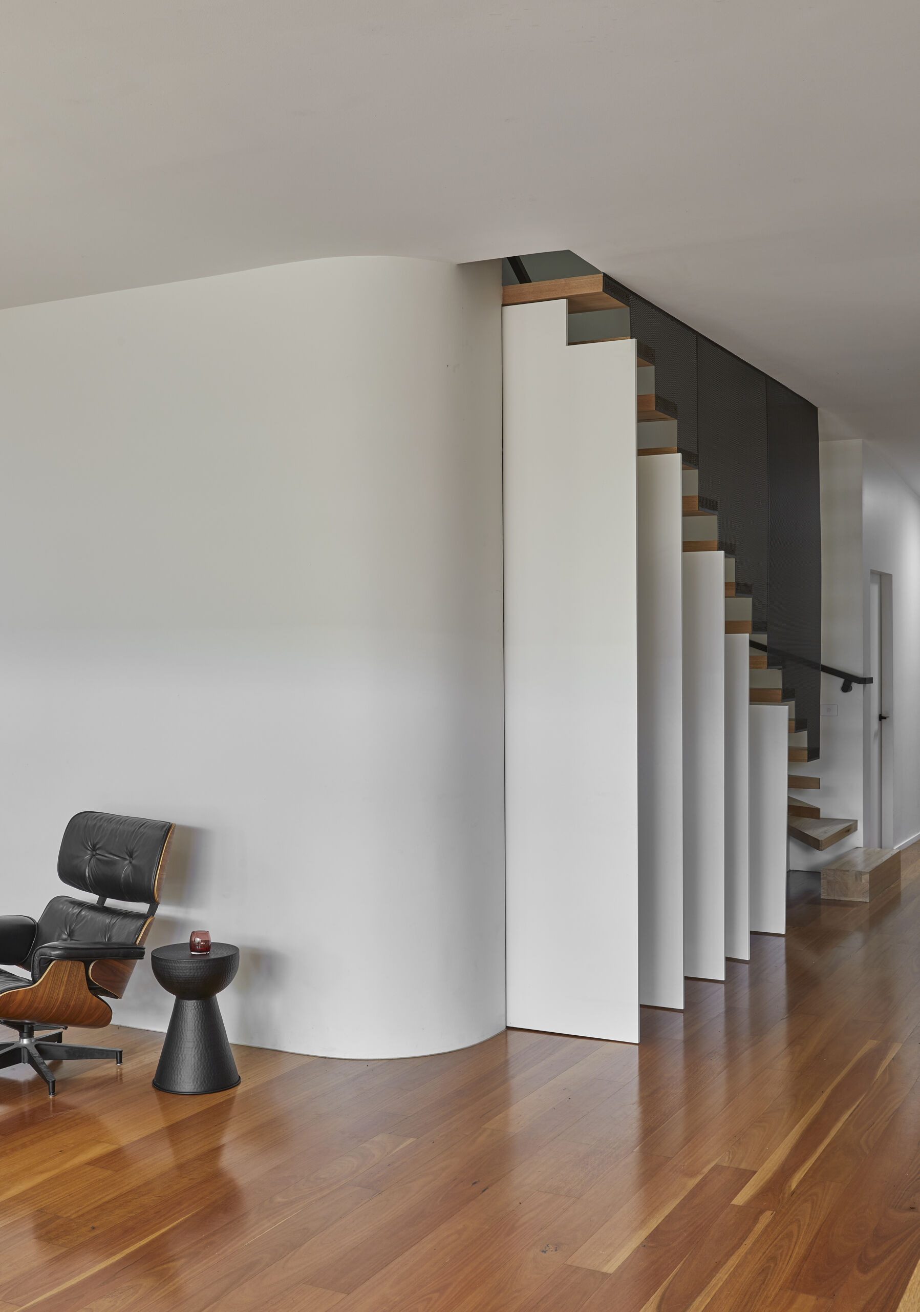 Tall white cabinet doors open outward beneath a modern timber staircase, revealing how concealed under-stair storage is integrated into the stepped design.