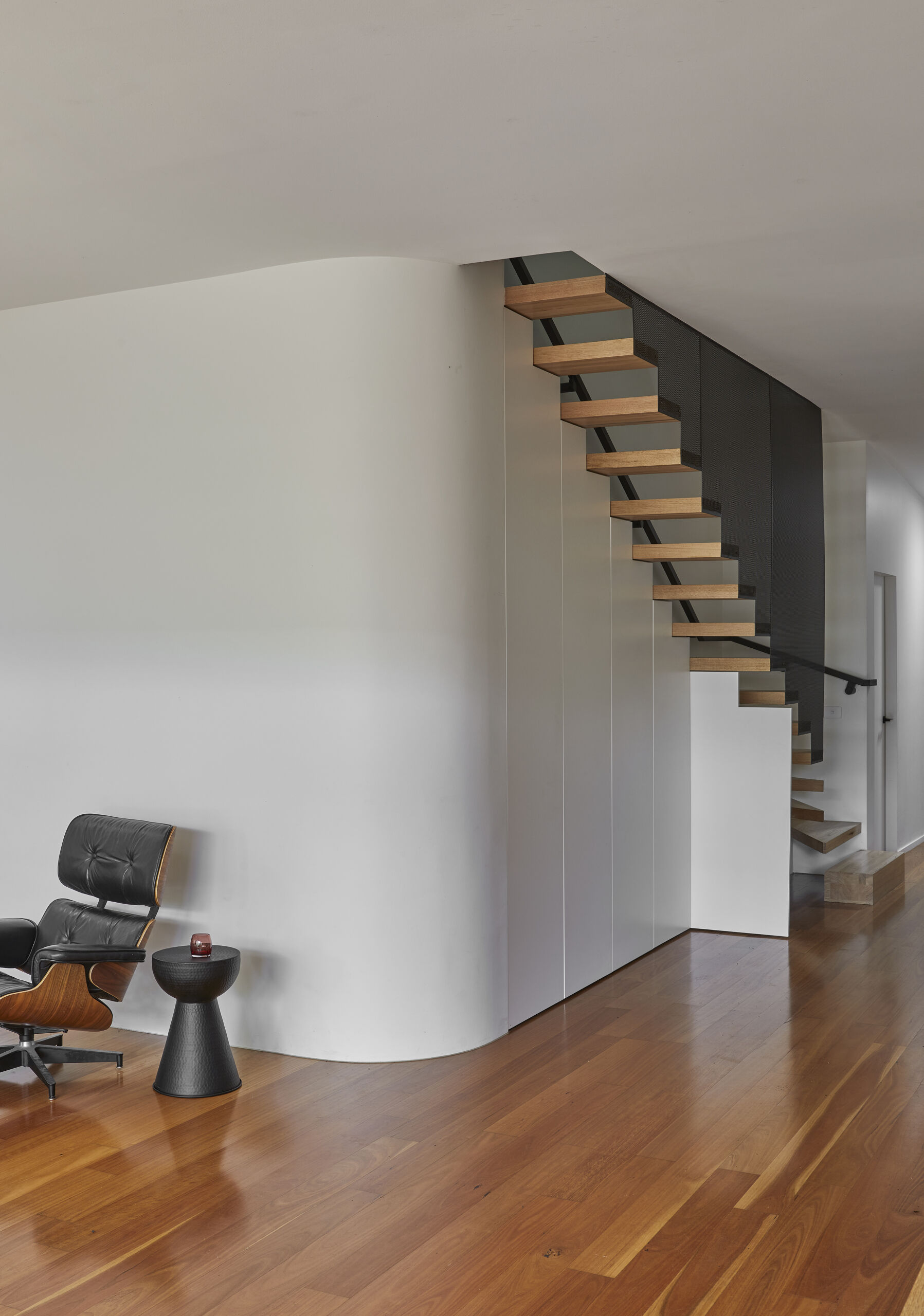 A contemporary staircase with timber treads and a black metal screen incorporates concealed storage behind white doors, with one cabinet opened to reveal the hidden space.
