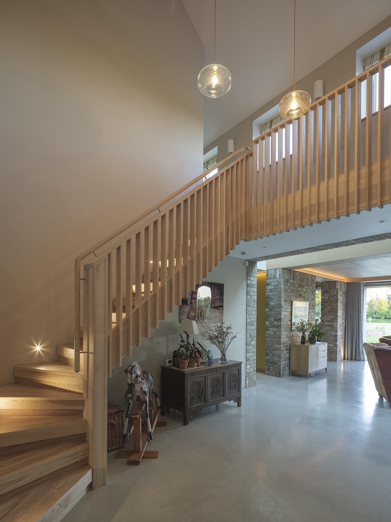 Exposed brick columns, pale wood stairs, large sliding glass doors, and polished concrete floors bring natural textures into this contemporary open-plan home.