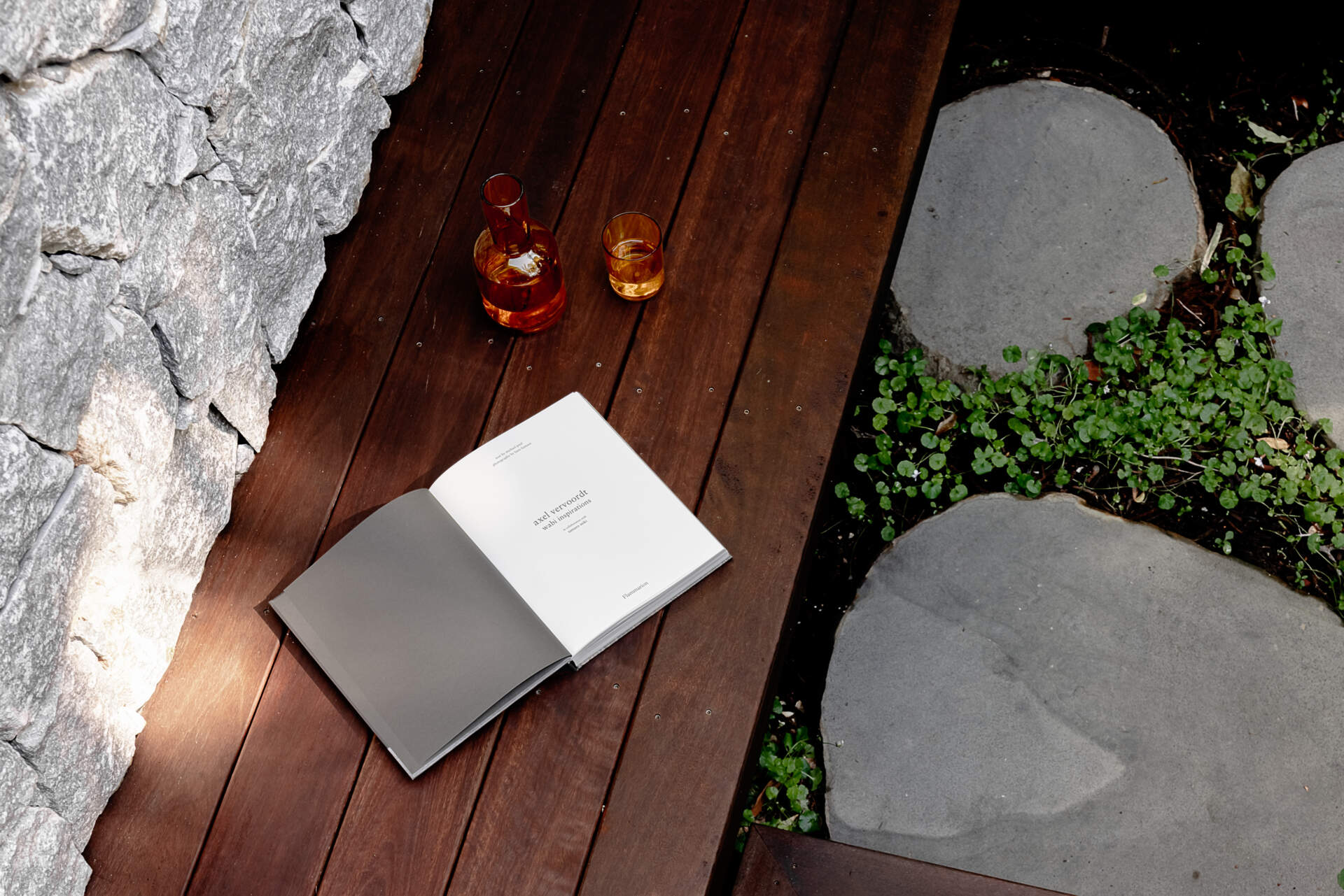 Explore the private patio at Raintree in Noosa Heads, designed by Void Building Design. A timber deck, built-in outdoor bench, natural stone walls, concrete stepping stones, and lush tropical landscaping create a secluded outdoor living space.