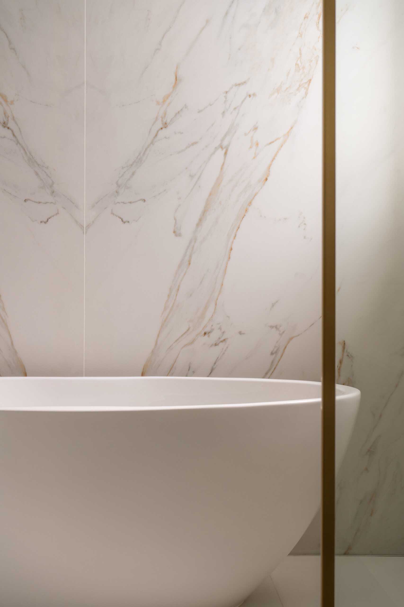Explore the luxurious primary bathroom at The White Arcade in Dubai. Featuring a freestanding oval bathtub, bookmatched marble feature wall, dual rainfall showers, brass bathroom fixtures, and built-in marble niches, this elegant bathroom was designed by D’Ora Tokai Designs.