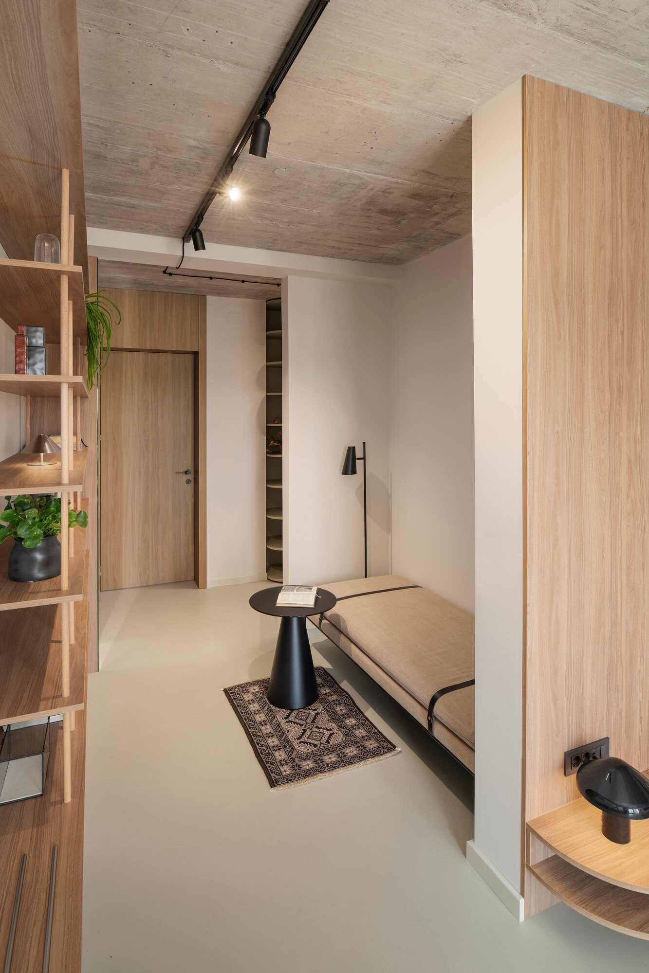 Tour the primary bedroom suite at Arc House in Croatia, featuring a timber platform bed, blue and green bedding, built-in wardrobes, a private sitting area, open wooden shelving and access to a covered terrace.