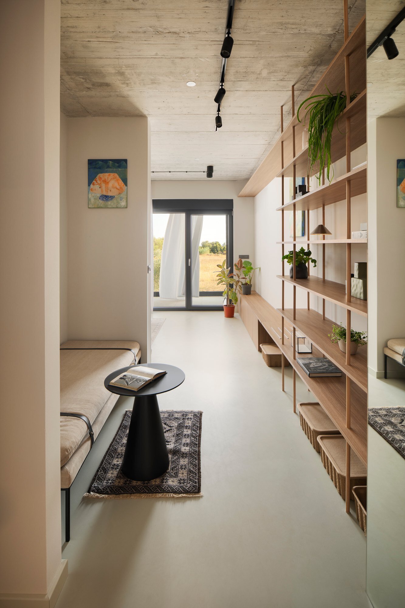 Tour the primary bedroom suite at Arc House in Croatia, featuring a timber platform bed, blue and green bedding, built-in wardrobes, a private sitting area, open wooden shelving and access to a covered terrace.