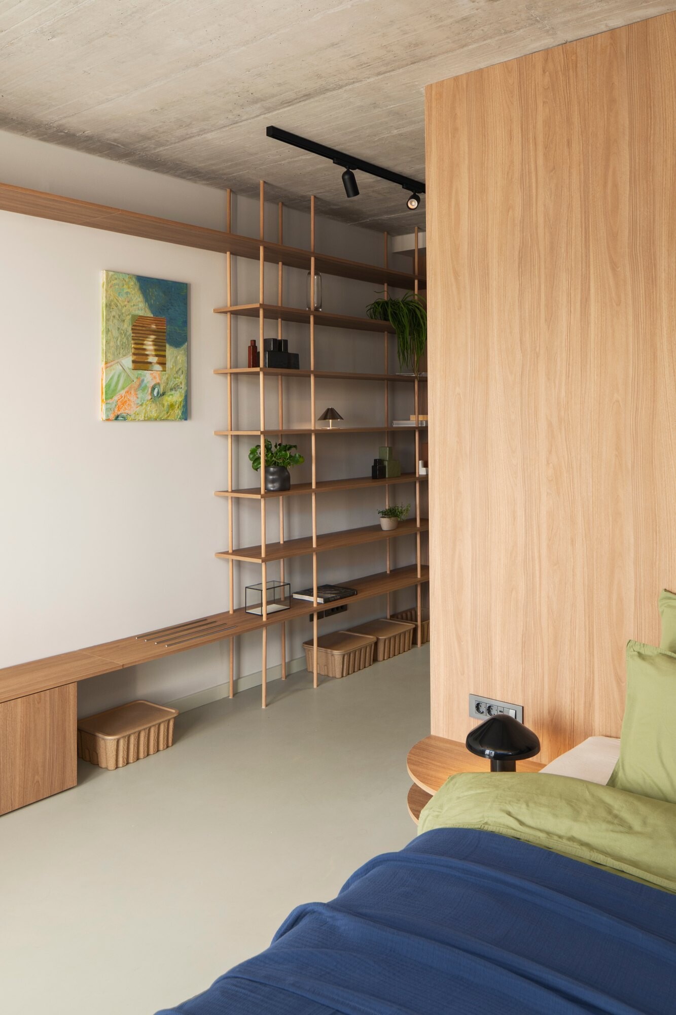 Tour the primary bedroom suite at Arc House in Croatia, featuring a timber platform bed, blue and green bedding, built-in wardrobes, a private sitting area, open wooden shelving and access to a covered terrace.