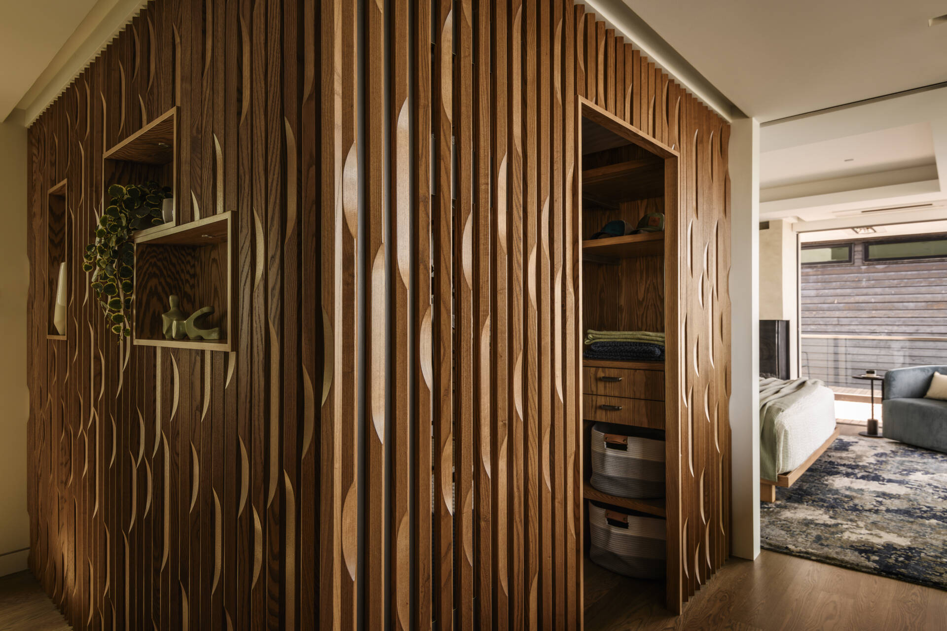 Sculptural vertical wood paneling, built-in storage niches, custom cabinetry, and a long countertop beneath lake-facing windows create a modern walk-in closet with plenty of character.