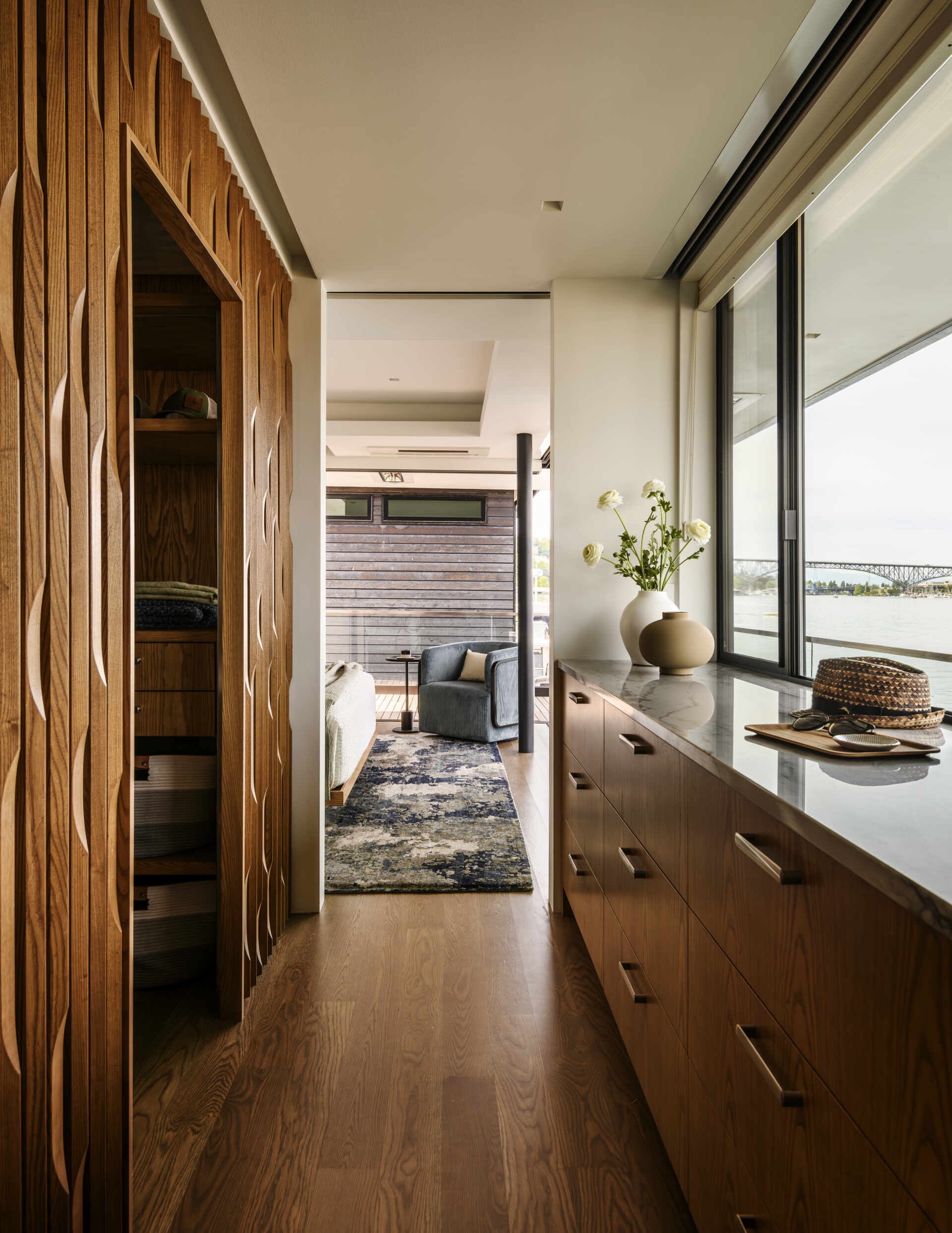 Sculptural vertical wood paneling, built-in storage niches, custom cabinetry, and a long countertop beneath lake-facing windows create a modern walk-in closet with plenty of character.