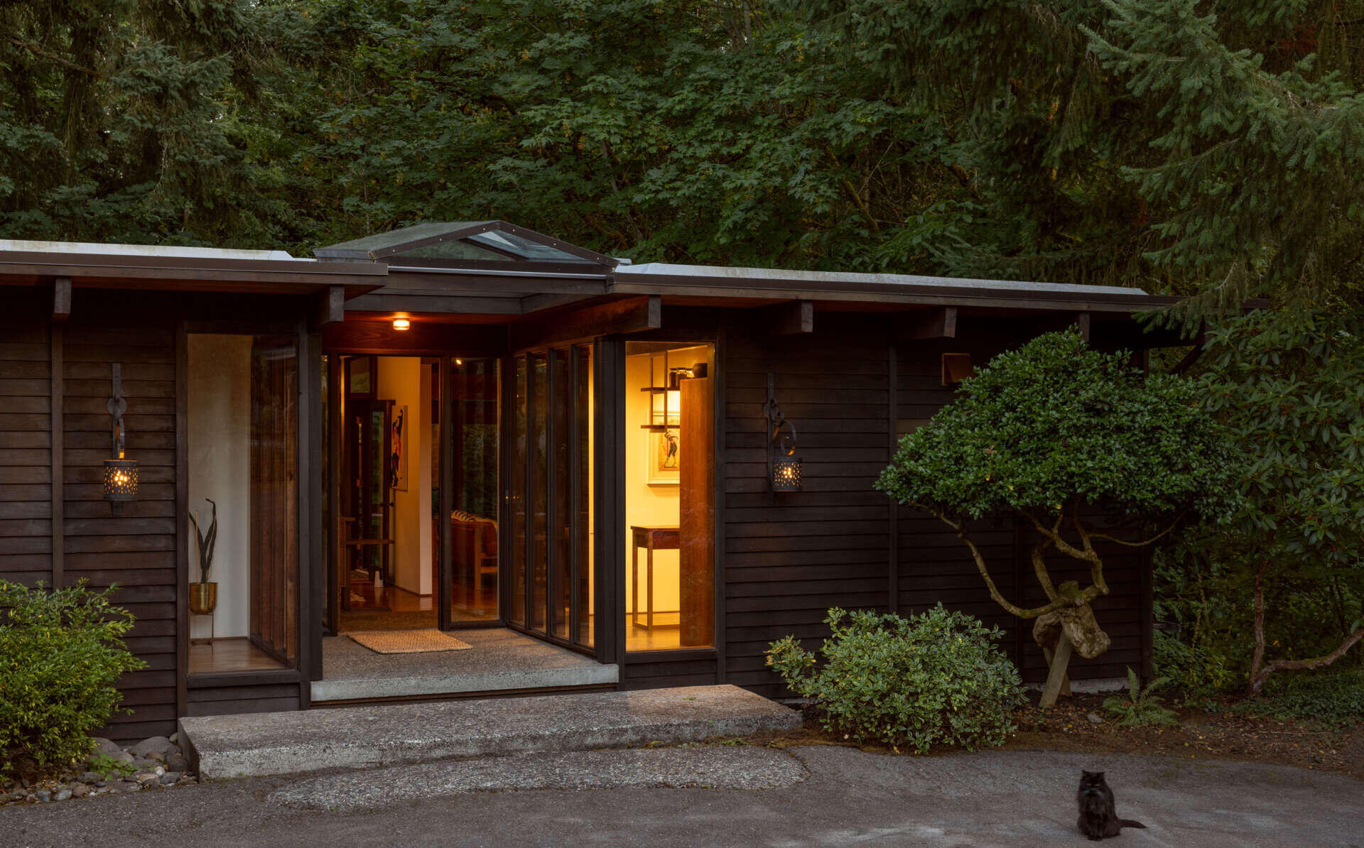 Step inside The Burrows, a renovated mid-century home in Seattle by chadbourne + doss architects. A recessed entrance features floor-to-ceiling glass, exposed timber ceilings, a concrete landing, and a custom walnut room divider.