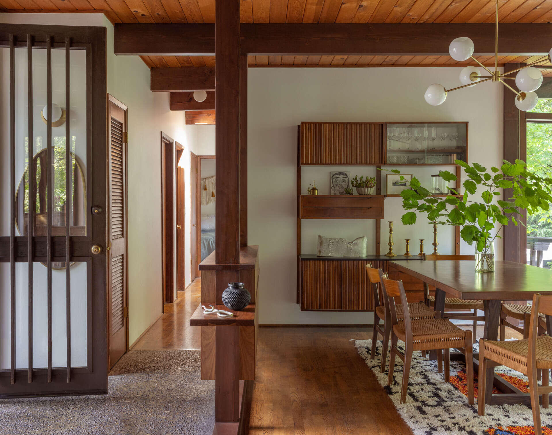 Explore the dining room of The Burrows, a mid-century Seattle home renovated by chadbourne + doss architects. Wooden furniture, woven dining chairs, a brass globe chandelier, and vintage-style cabinetry create a warm interior.