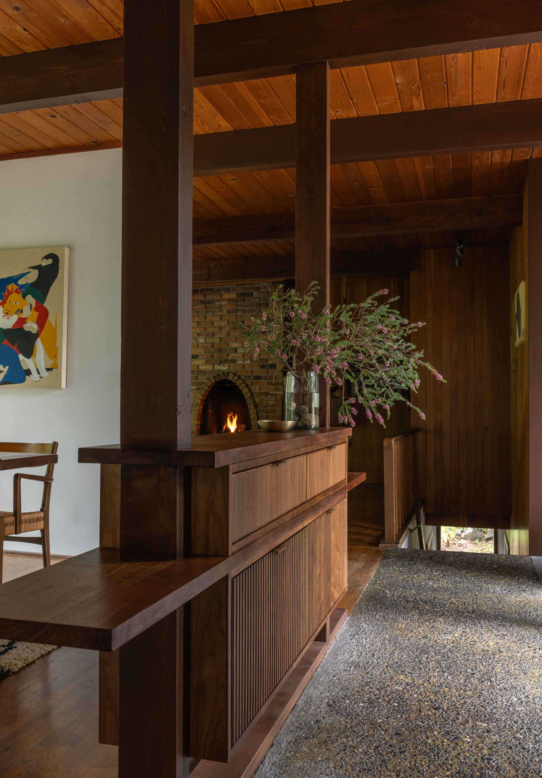 Step inside The Burrows, a renovated mid-century home in Seattle by chadbourne + doss architects. A recessed entrance features floor-to-ceiling glass, exposed timber ceilings, a concrete landing, and a custom walnut room divider.