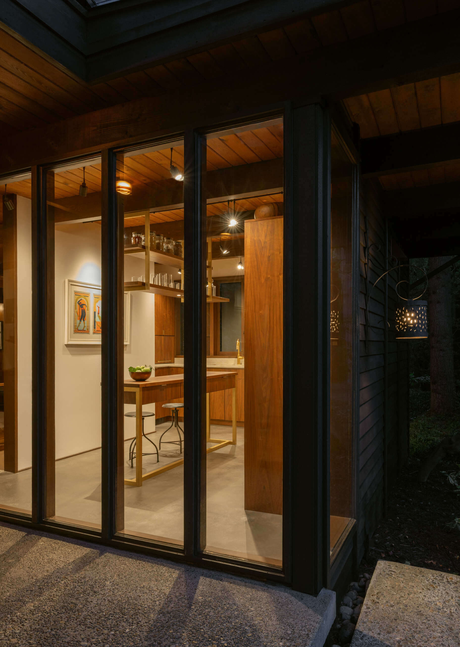 Explore the renovated kitchen of The Burrows, a mid-century modern home in Seattle by chadbourne + doss architects. Custom walnut cabinetry, slatted wood details, brass fixtures, pale stone countertops, a brass chef's sink, and a sculptural kitchen island bring warmth and functionality to the space.