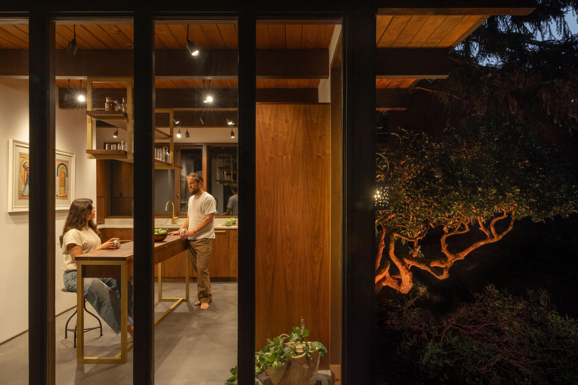Explore the renovated kitchen of The Burrows, a mid-century modern home in Seattle by chadbourne + doss architects. Custom walnut cabinetry, slatted wood details, brass fixtures, pale stone countertops, a brass chef's sink, and a sculptural kitchen island bring warmth and functionality to the space.