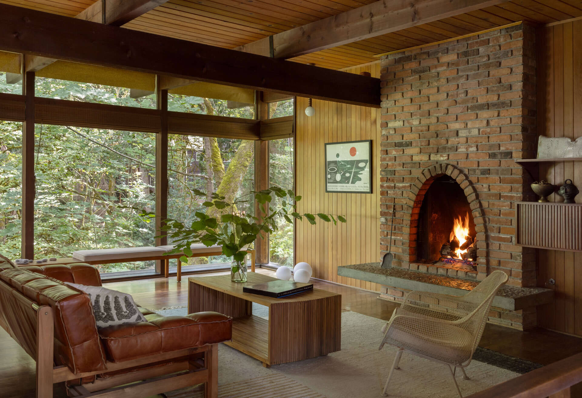 Take a look inside the living room of the Burrows, a renovated mid-century home in Seattle. An original arched brick fireplace, wood-paneled walls, exposed beams, vintage-inspired furniture, and a window bench give the space its warm, inviting character.