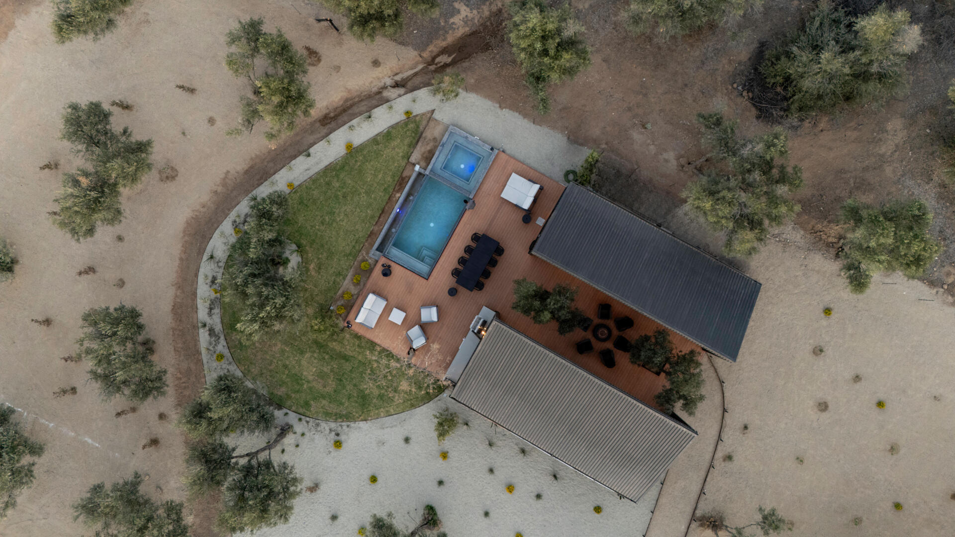 Explore the minimalist architecture of Serentha Cabin by ORTO STUDIO in Baja California, Mexico. Dark corrugated metal exteriors, sloping roofs, warm exterior lighting, gravel pathways, and olive trees create a modern rural cabin with an industrial edge.