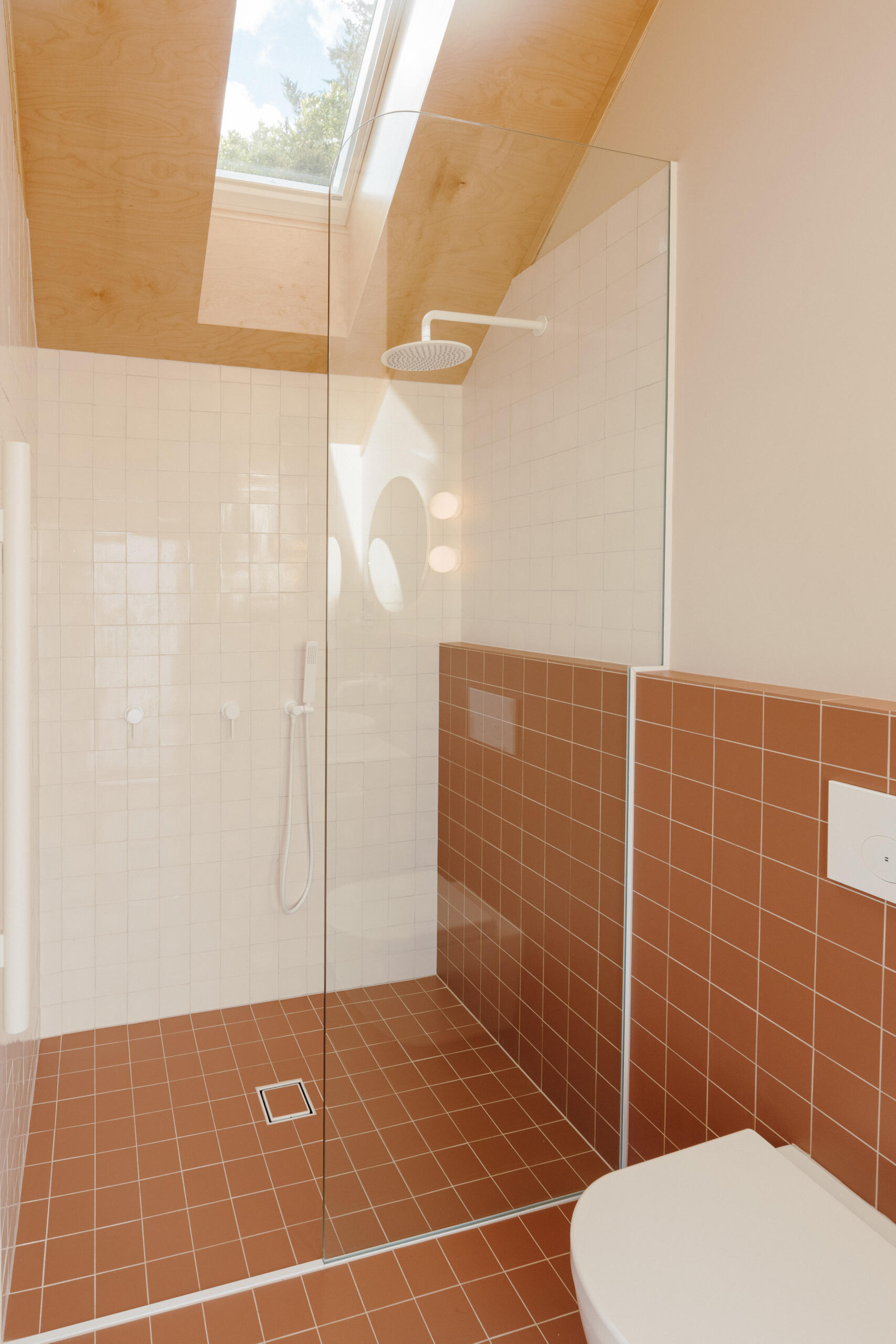 Discover a modern ensuite bathroom featuring terracotta square tiles, an arched doorway, a floating timber vanity, circular illuminated mirror and skylit walk-in shower. Small bathroom inspiration with warm colours and contemporary finishes.