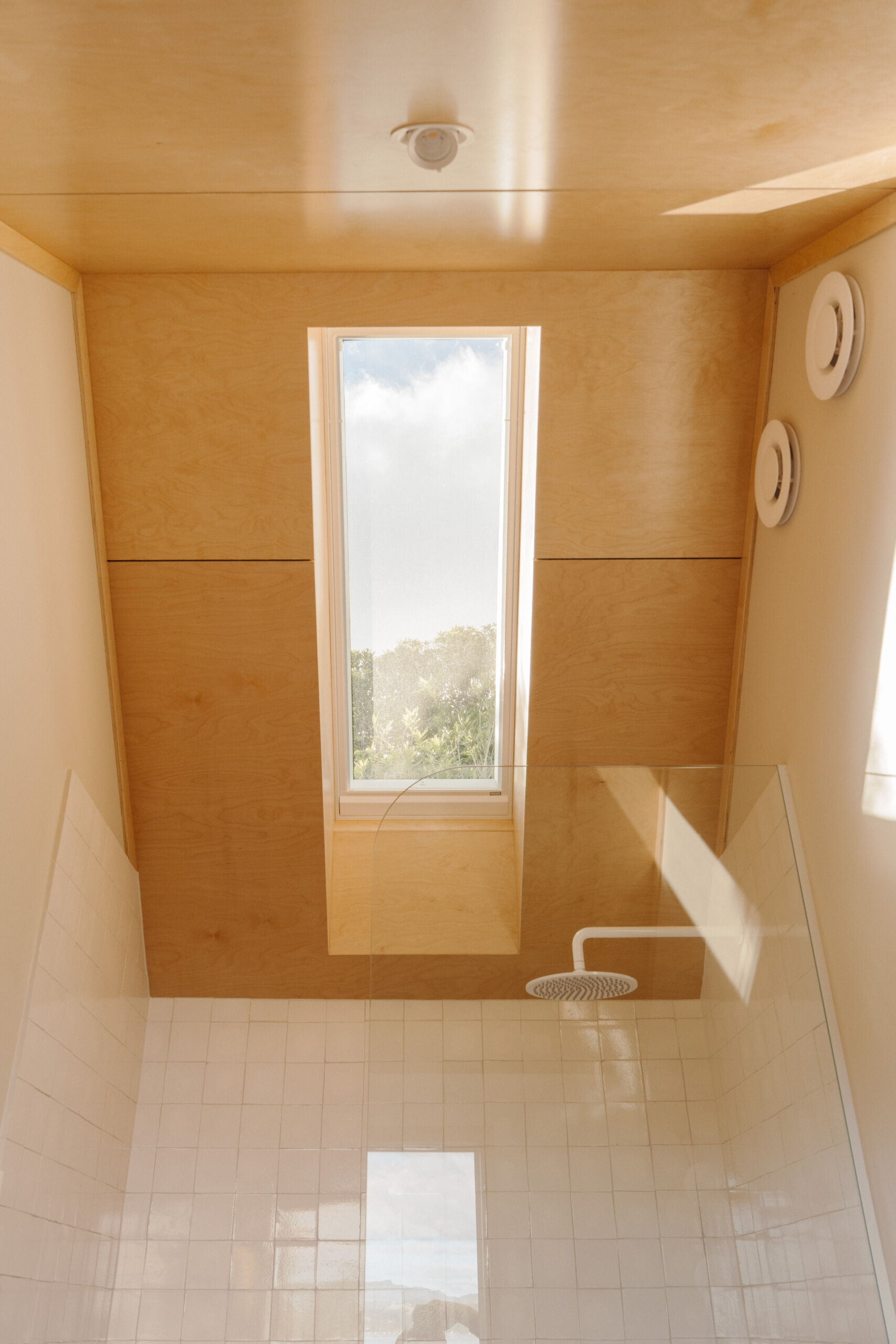 Discover a modern ensuite bathroom featuring terracotta square tiles, an arched doorway, a floating timber vanity, circular illuminated mirror and skylit walk-in shower. Small bathroom inspiration with warm colours and contemporary finishes.