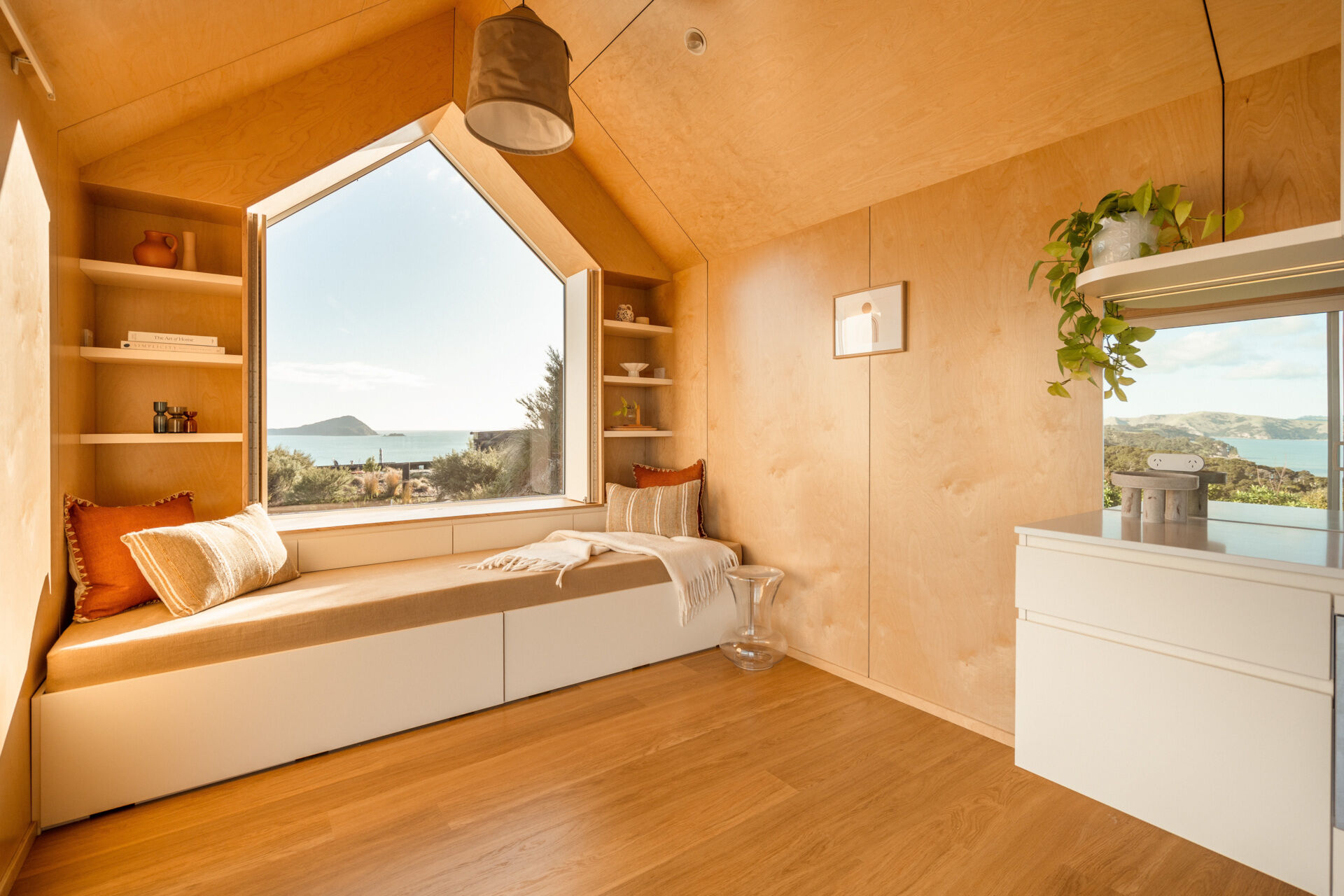 Inside Arc's small coastal cabin, a beautiful birch plywood living room features a built-in window bench, hidden guest sleeping space, open shelving and panoramic harbour views. Inspiration for small living rooms and window seat designs.