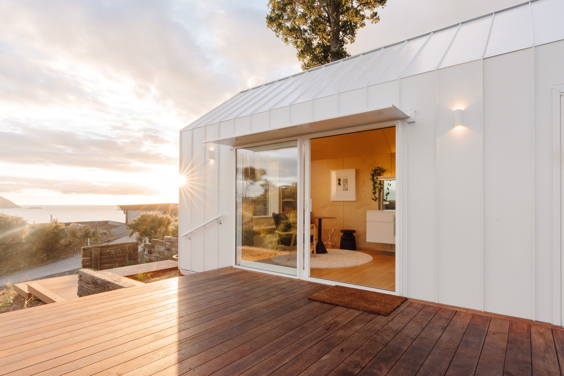 Discover the architecture of Arc's Wyuna Bay cabin in New Zealand, featuring white standing-seam metal cladding, a gabled roof, expansive glazing and timber decking overlooking Coromandel Harbour.