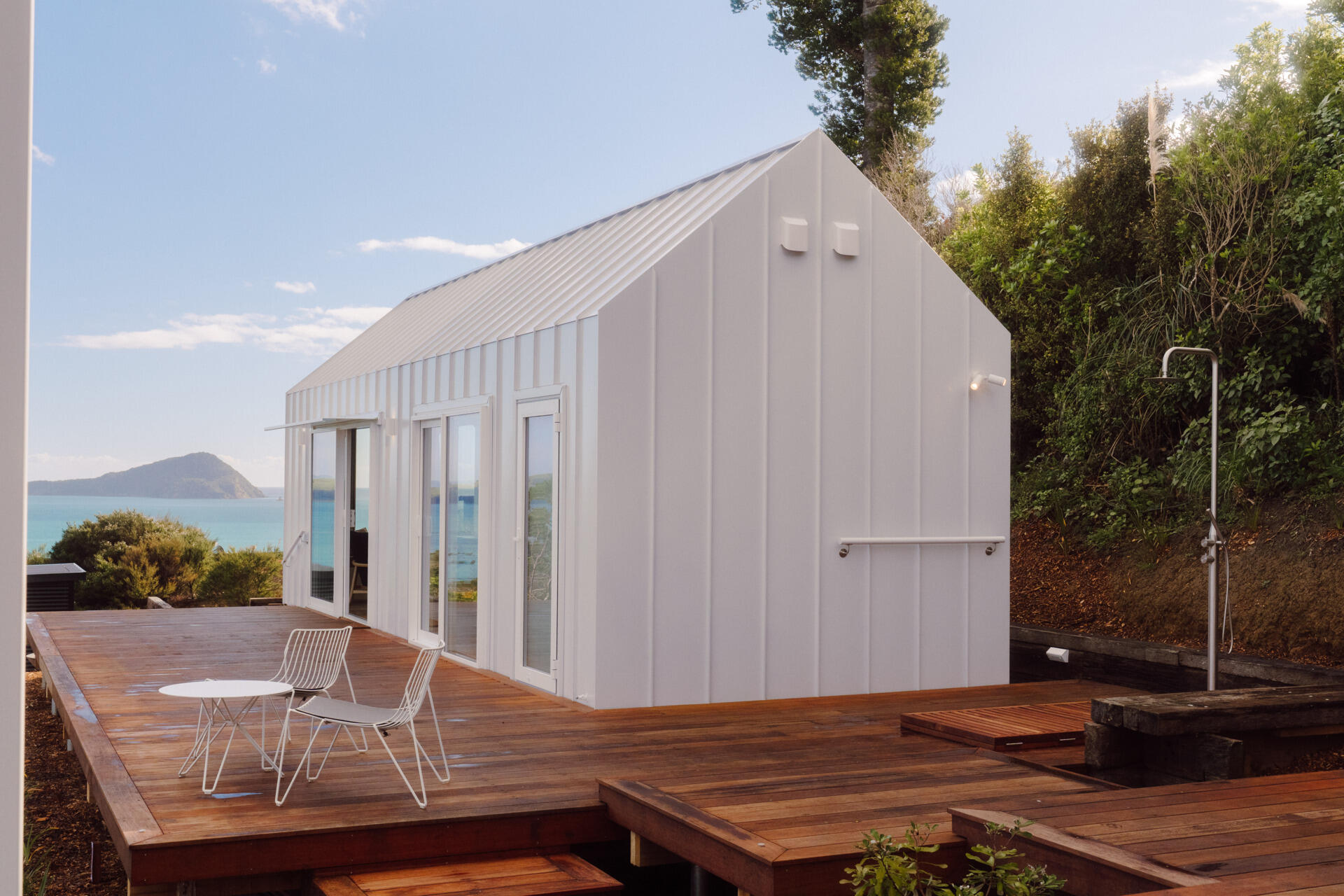 Discover the architecture of Arc's Wyuna Bay cabin in New Zealand, featuring white standing-seam metal cladding, a gabled roof, expansive glazing and timber decking overlooking Coromandel Harbour.