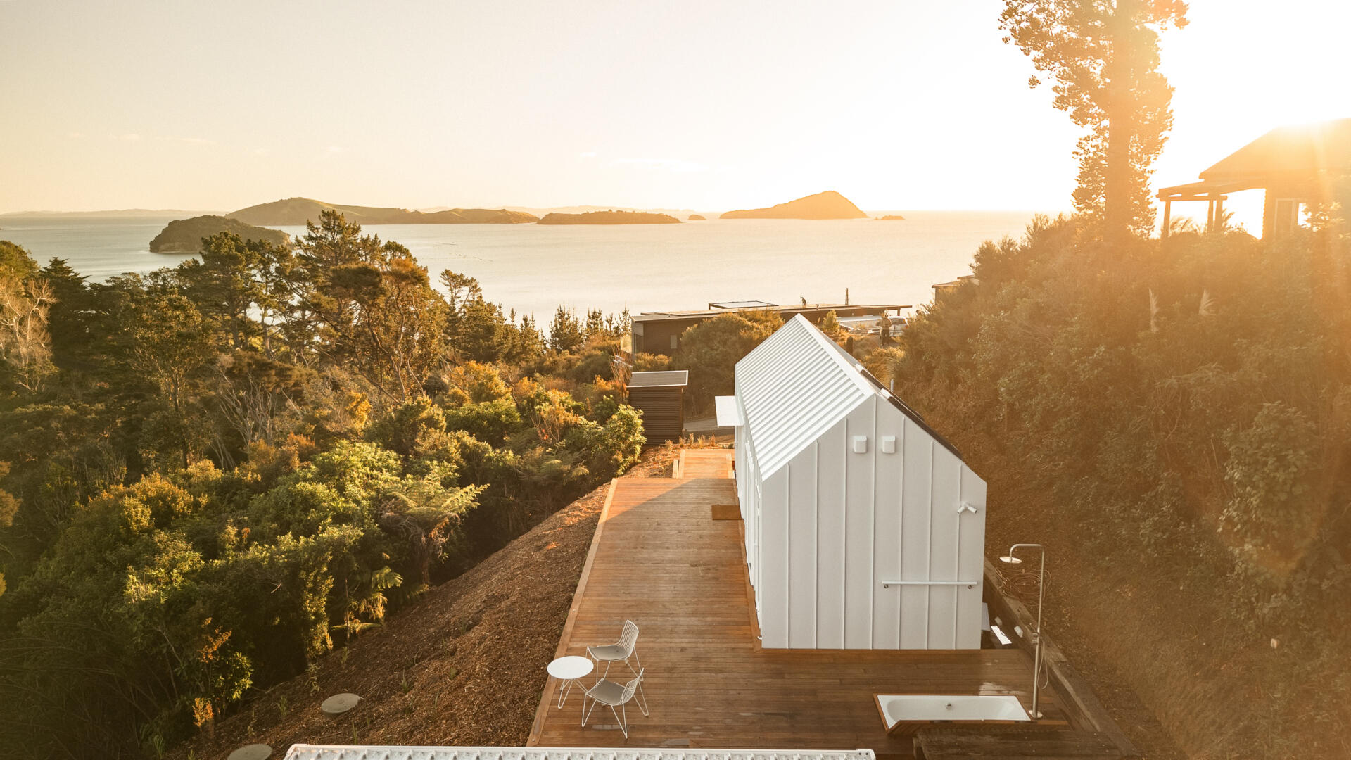Discover the architecture of Arc's Wyuna Bay cabin in New Zealand, featuring white standing-seam metal cladding, a gabled roof, expansive glazing and timber decking overlooking Coromandel Harbour.