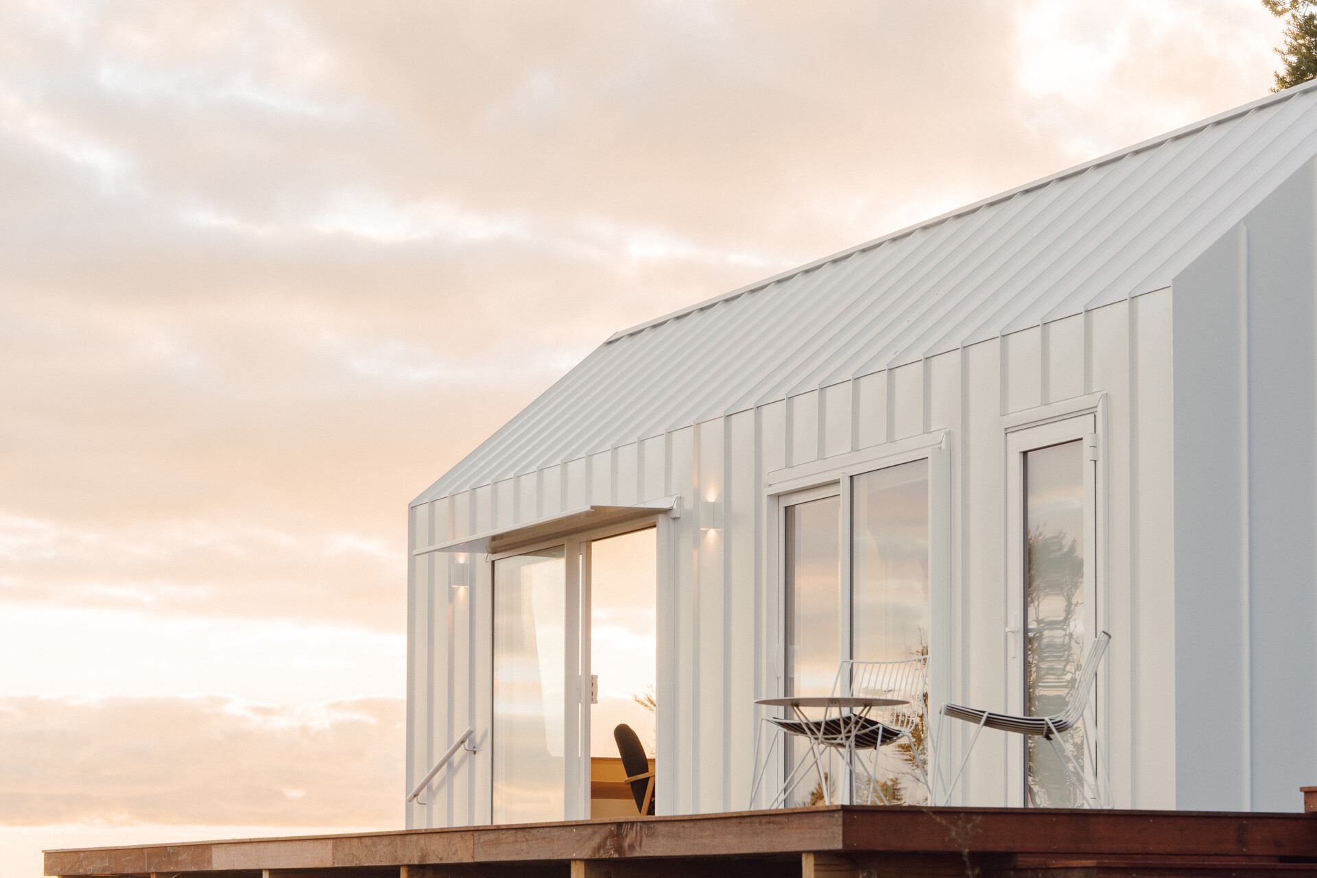 Discover the architecture of Arc's Wyuna Bay cabin in New Zealand, featuring white standing-seam metal cladding, a gabled roof, expansive glazing and timber decking overlooking Coromandel Harbour.