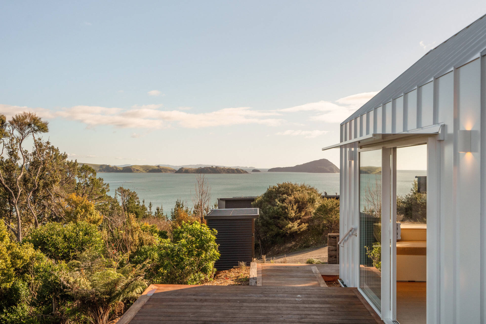 Discover the architecture of Arc's Wyuna Bay cabin in New Zealand, featuring white standing-seam metal cladding, a gabled roof, expansive glazing and timber decking overlooking Coromandel Harbour.