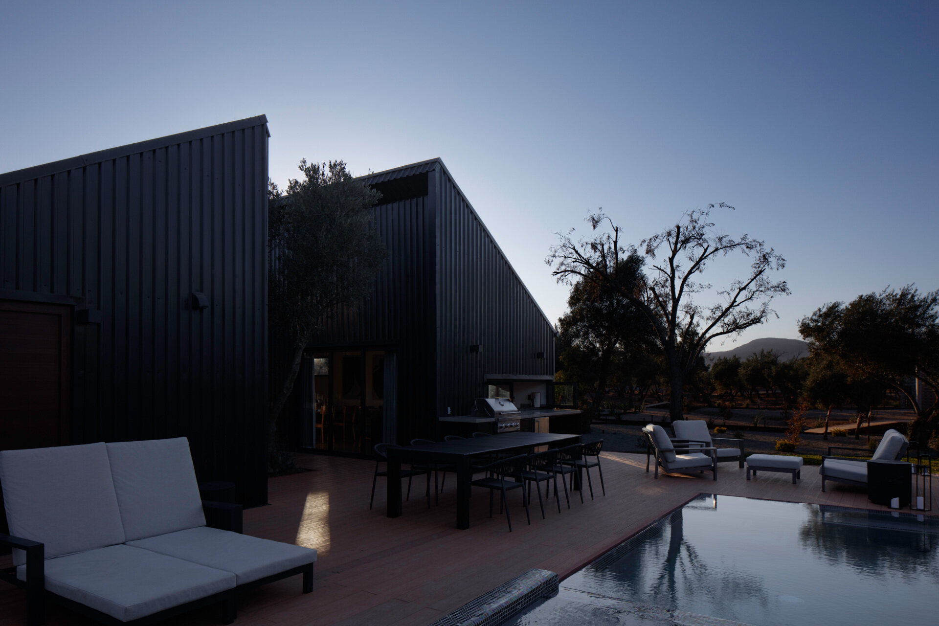 Discover the modern swimming pool at Serentha Cabin by ORTO STUDIO in Baja California, Mexico. A rectangular pool with blue mosaic tiles, a smaller raised pool, timber decking, and scenic olive grove views creates an inviting outdoor space.