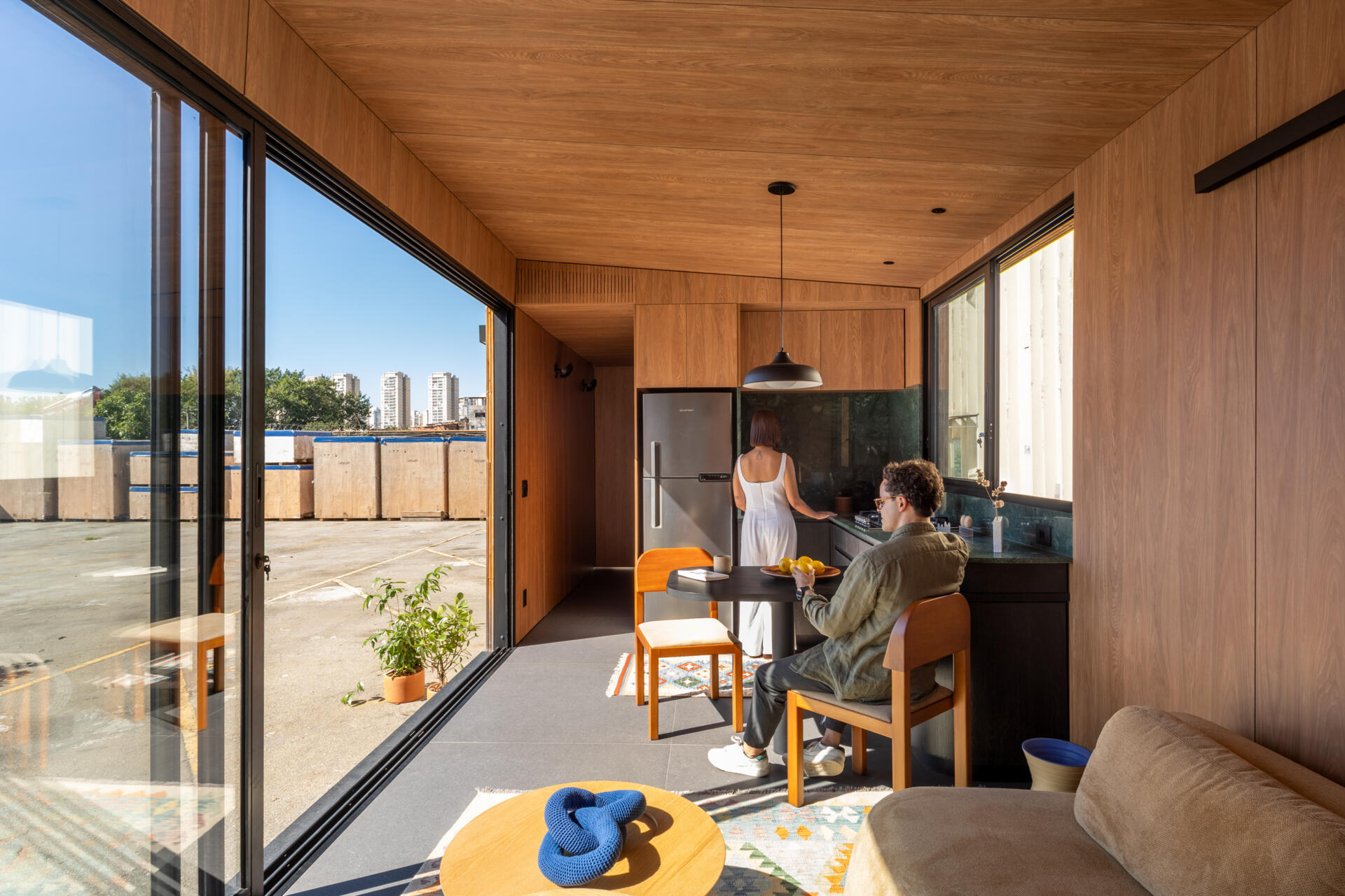 Explore the space-saving layout of Casa M38, a small prefab home with an open kitchen and living room, an integrated dining table, a private bedroom with a workspace, and a bathroom.