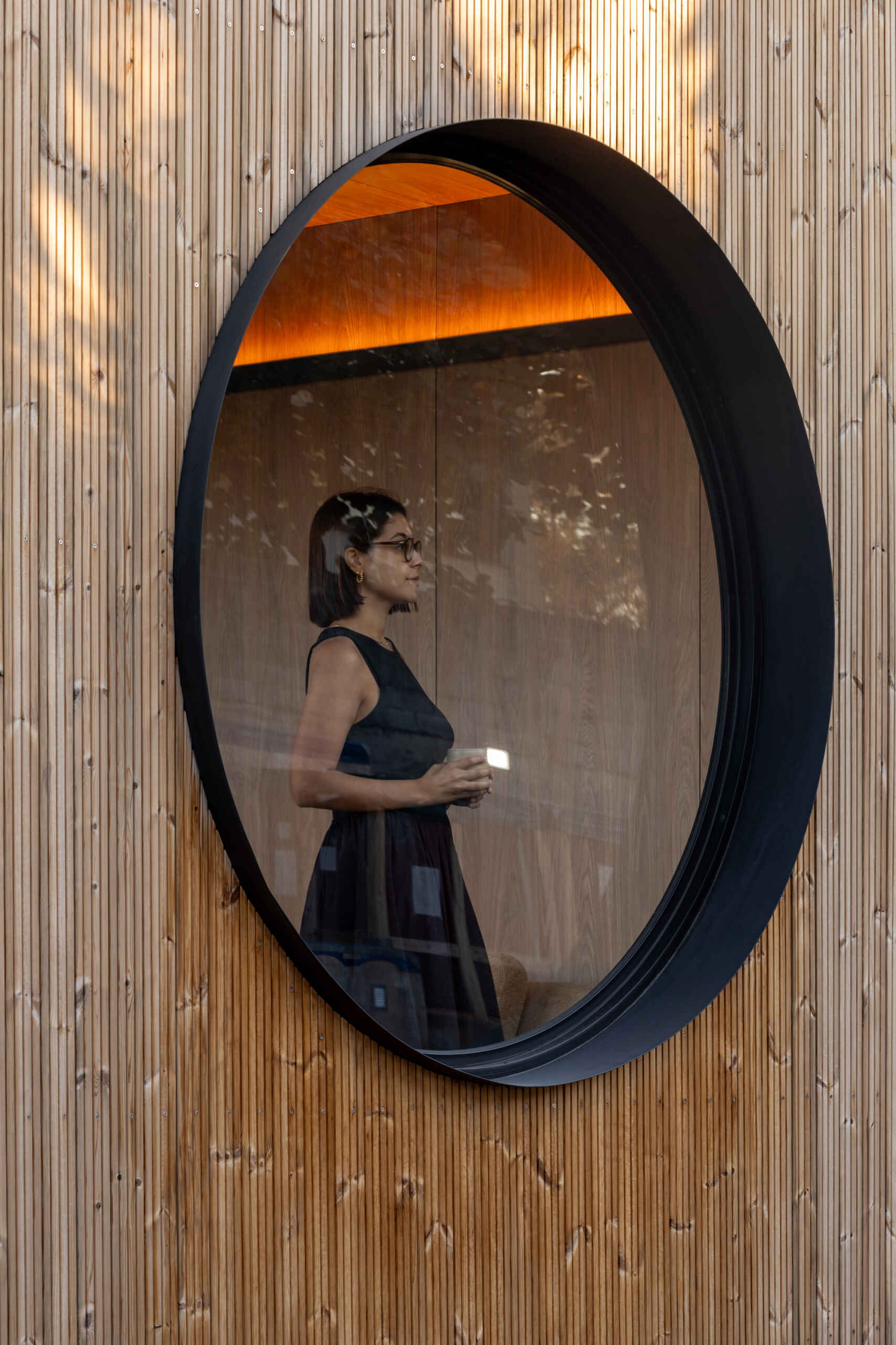 This small prefabricated house features vertical wood cladding, large sliding glass doors, and distinctive circular windows at both ends.