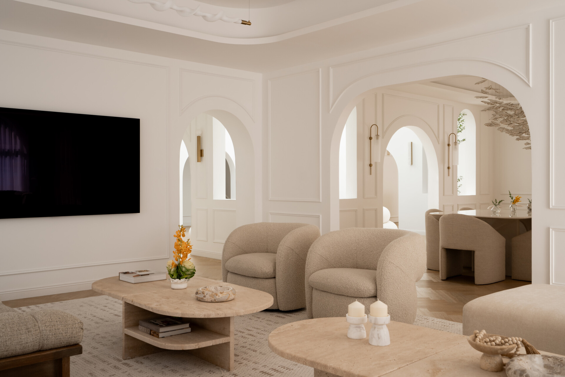 Step inside the media room of The White Arcade in Dubai. A large curved sectional sofa, bouclé armchairs, stone coffee tables, textured rug, and arched windows create a cosy yet sophisticated neutral living room designed by D’Ora Tokai Designs.