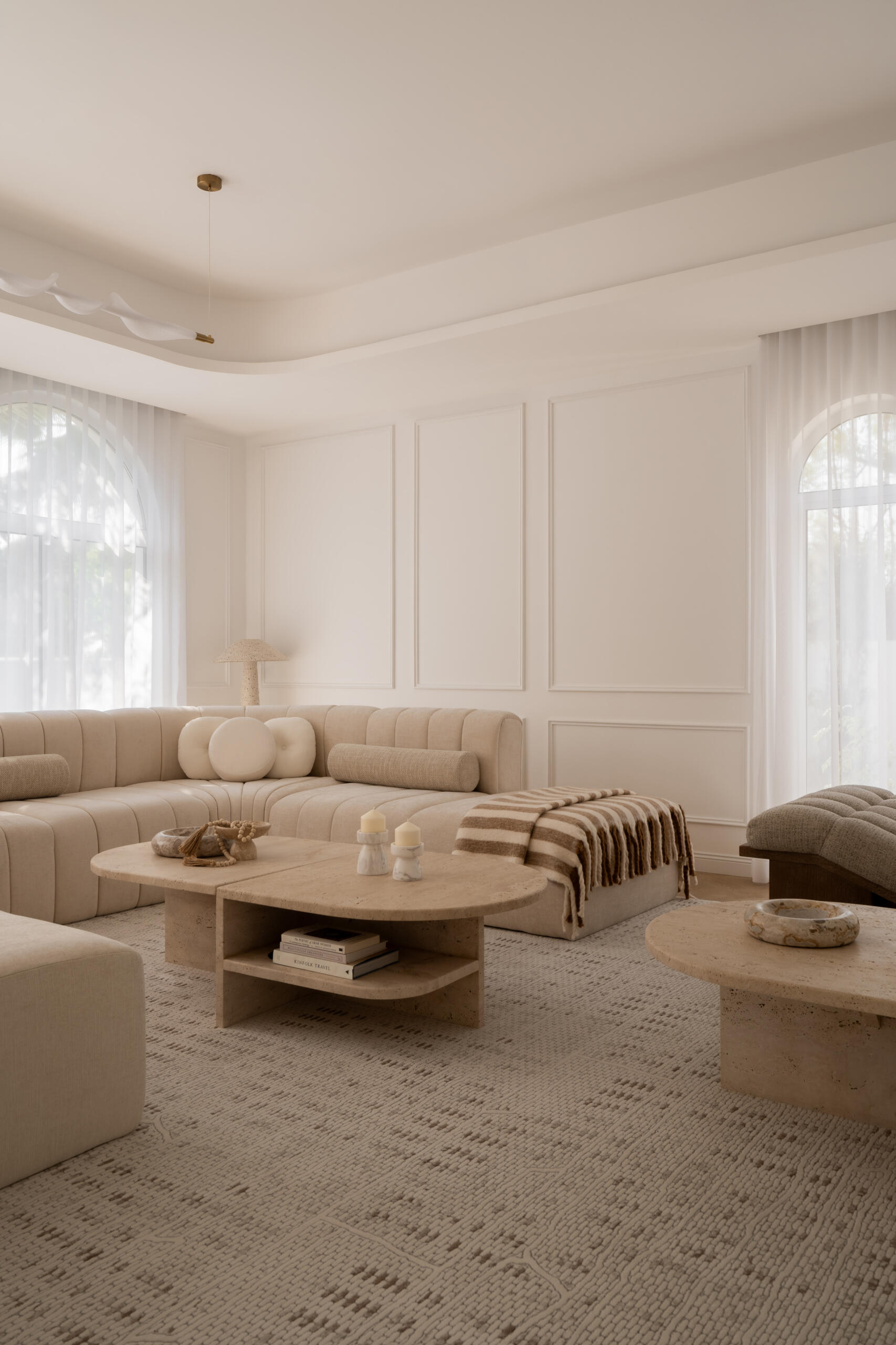 Step inside the media room of The White Arcade in Dubai. A large curved sectional sofa, bouclé armchairs, stone coffee tables, textured rug, and arched windows create a cosy yet sophisticated neutral living room designed by D’Ora Tokai Designs.