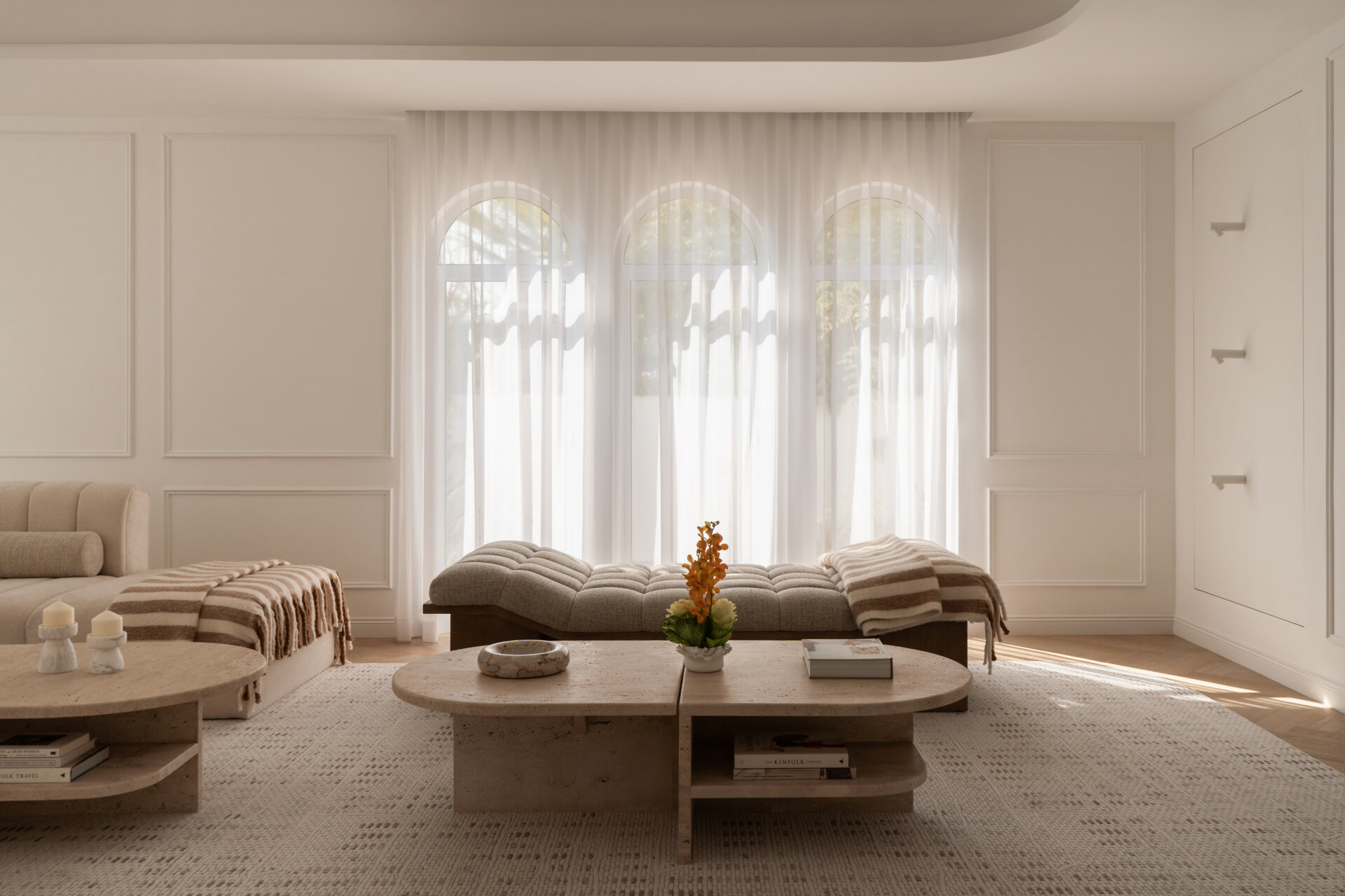 Step inside the media room of The White Arcade in Dubai. A large curved sectional sofa, bouclé armchairs, stone coffee tables, textured rug, and arched windows create a cosy yet sophisticated neutral living room designed by D’Ora Tokai Designs.