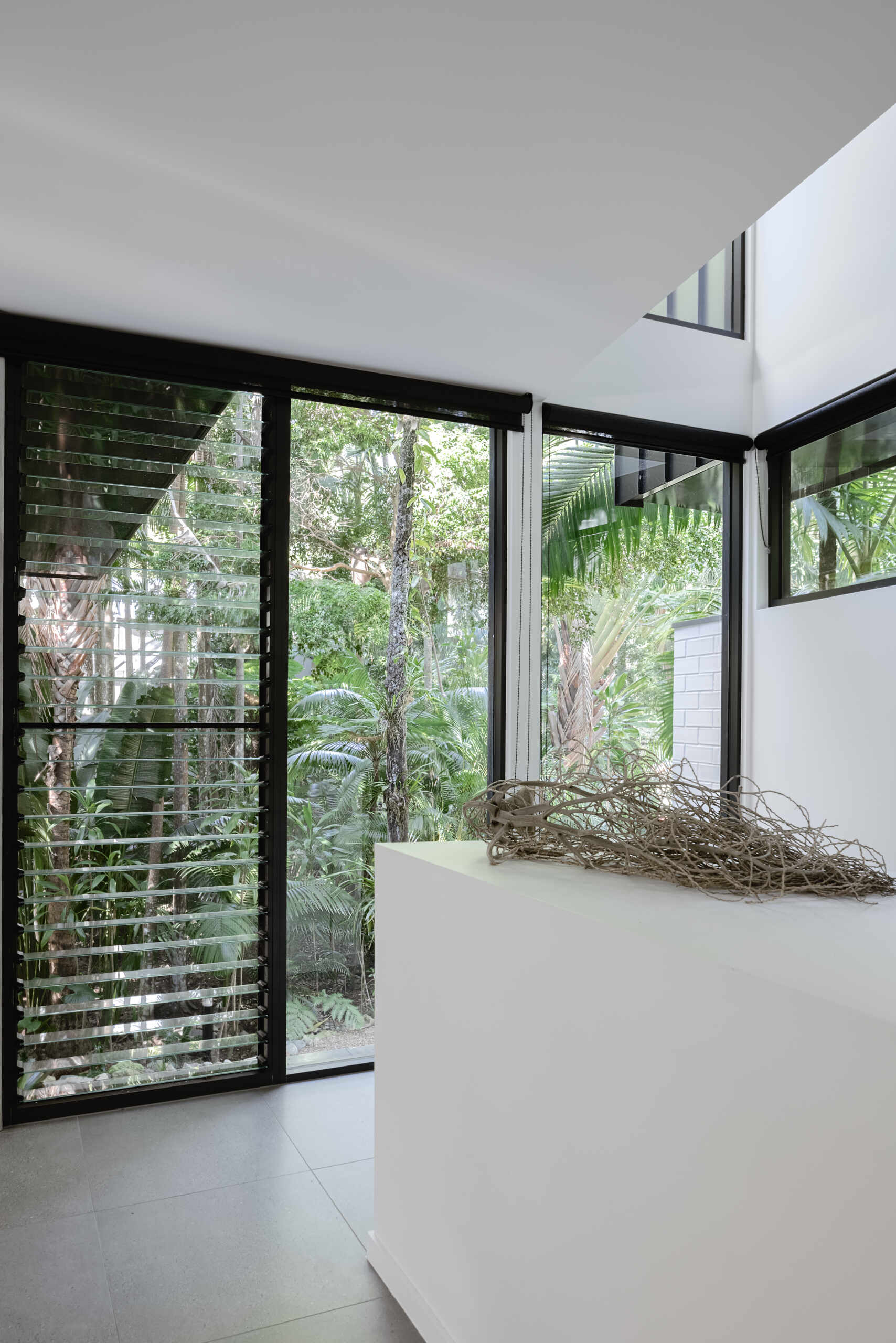 Explore the windows and staircase at Raintree in Noosa Heads, Australia, designed by Void Building Design. Floor-to-ceiling glazing, timber stairs, glass balustrades, and tropical forest views create a bright, modern interior.